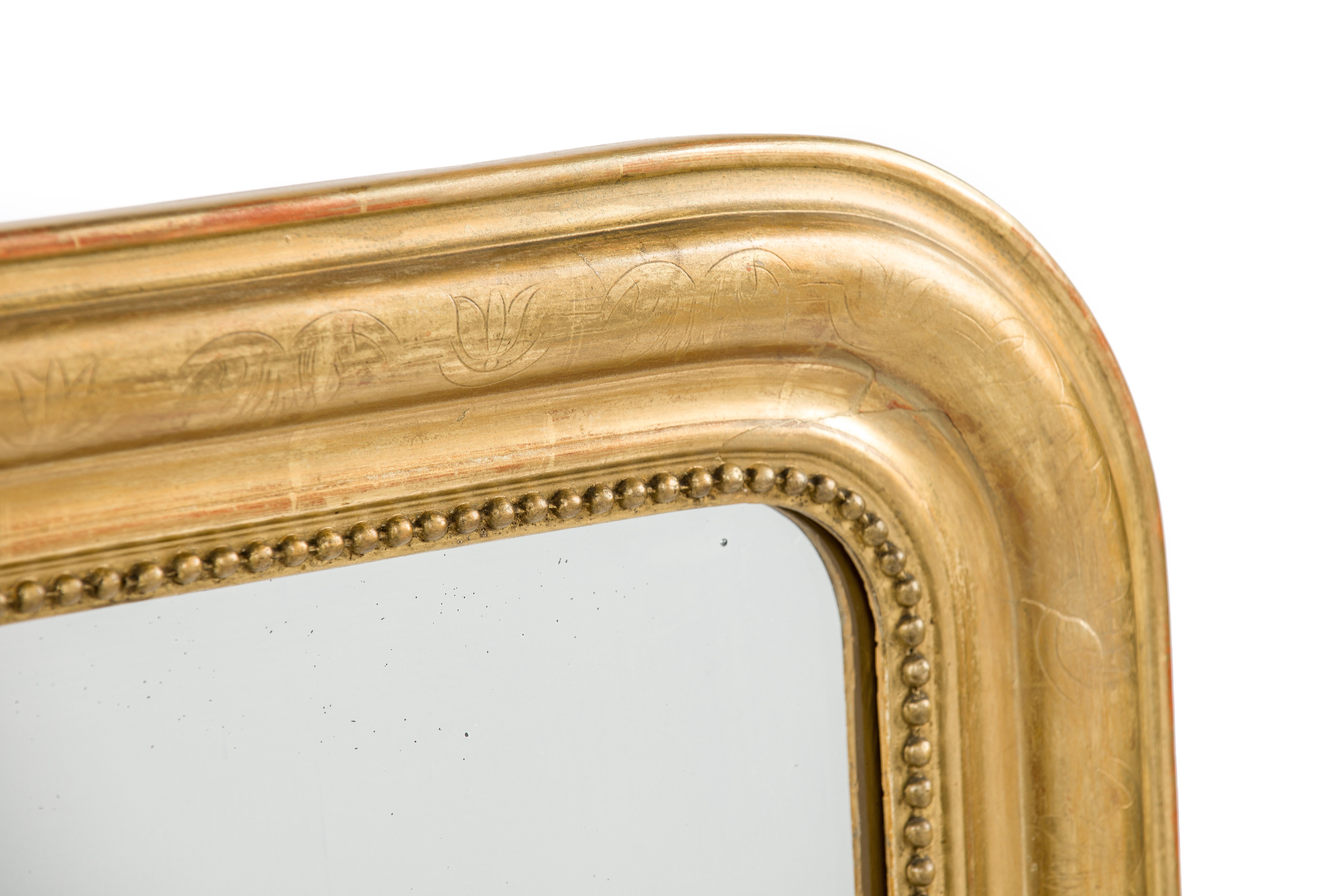 This is a beautiful completely gold leaf gilt Louis Philippe mirror. It features the upper rounded corners typical for Louis Philippe mirrors. The frame is decorated with a floral engraving on the most elevated part of the frame. A pearl beading