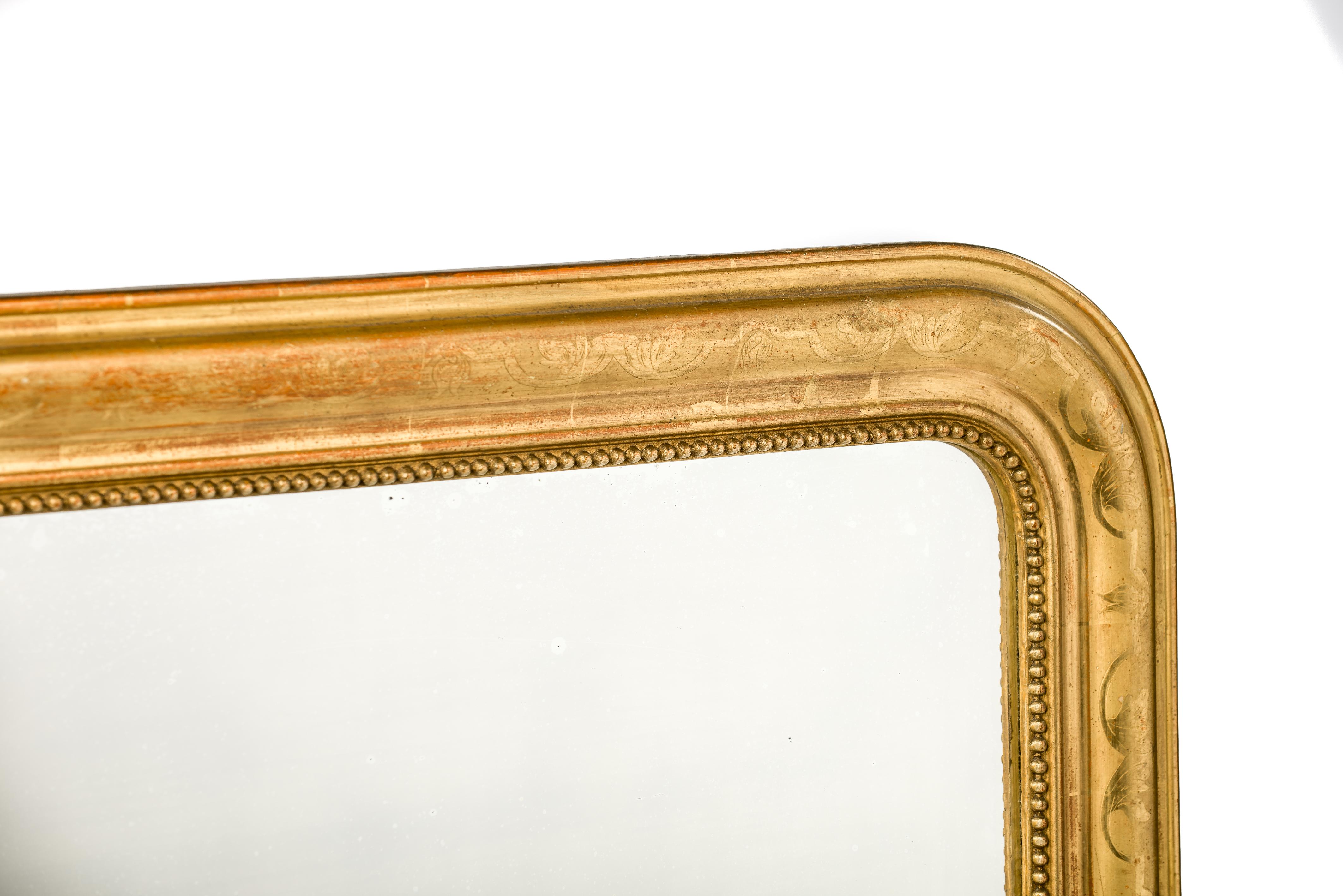 This is a beautiful completely gold leaf gilt Louis Philippe mirror. It features the upper rounded corners typical for Louis Philippe mirrors. The frame is decorated with a floral engraving on the most elevated part of the frame. A pearl beading