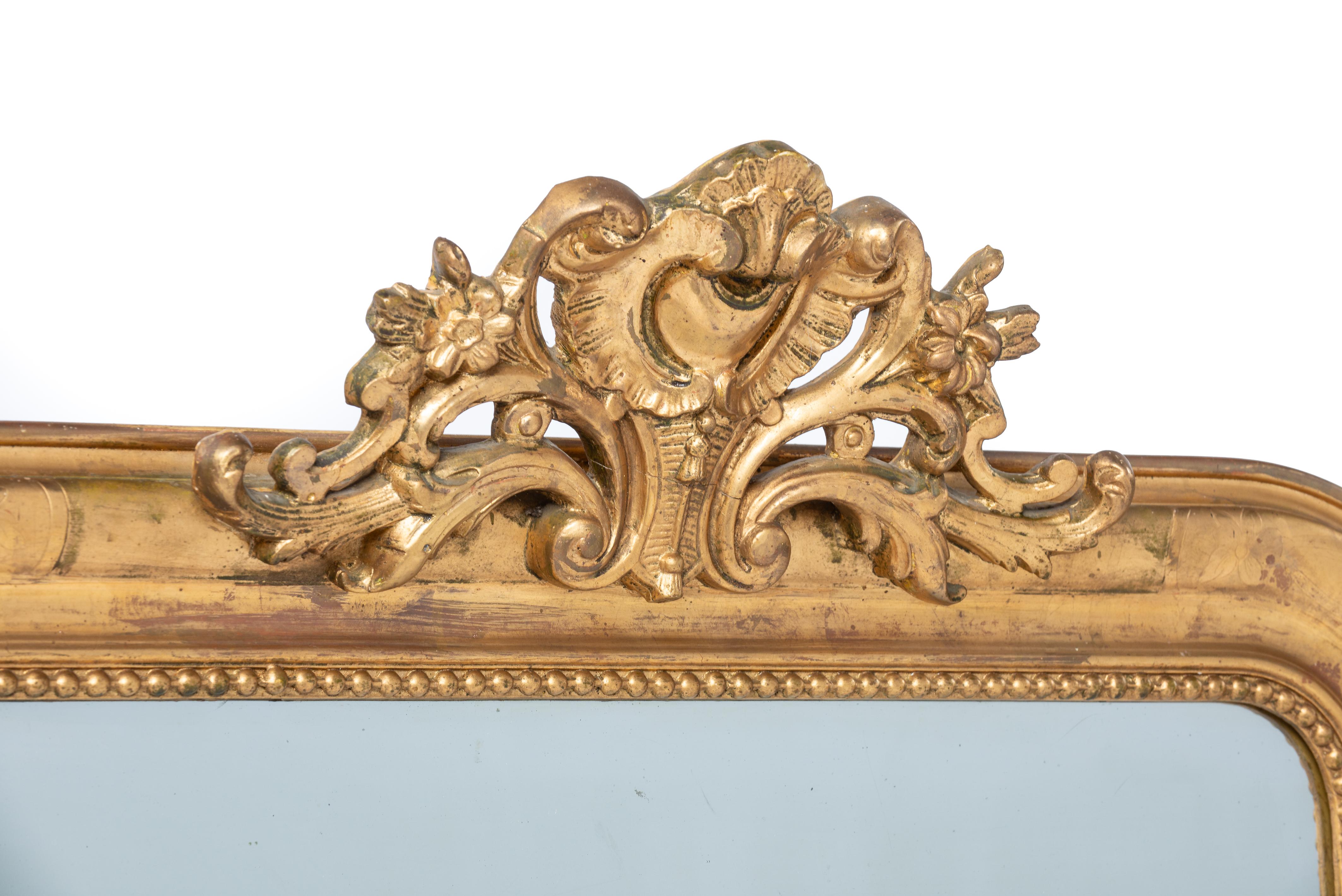 This is a wonderful completely gold leaf gilt mirror that was made in central France in the late 19th century, circa 1875. It features the upper rounded corners typical for the Louis Philippe style. The mirror was decorated with an ornate crest