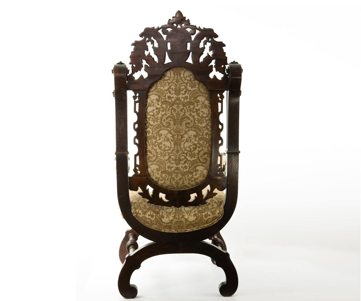 This antique Savonarola style upholstered chair is rare in the fact that the popular style is not often seen in such a fine high back. The carvings includes lion heads both on the arms and on the front of the chair, griffins on the back rest and a