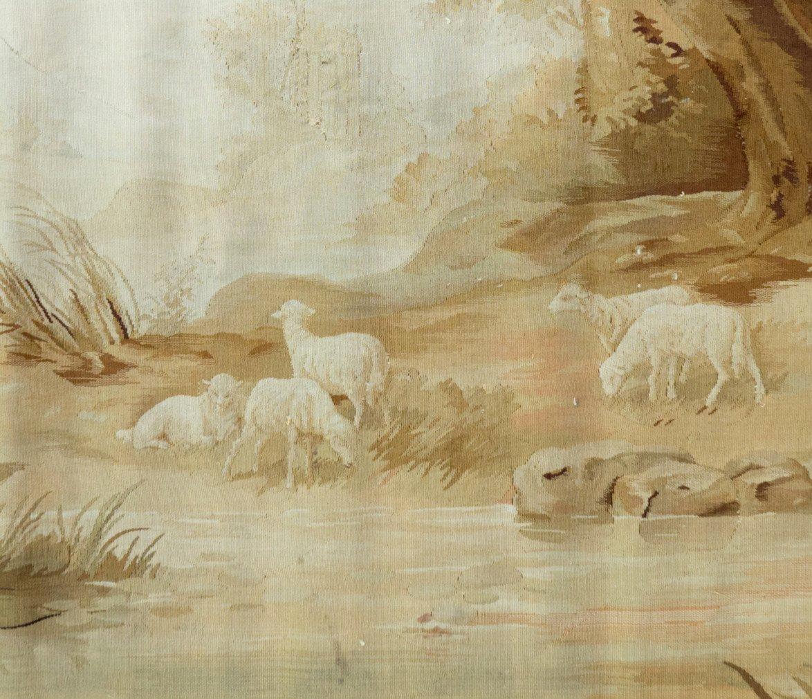 Antique 19th century French landscape Verdure tapestry depicting a lovely setting on the sheep on the banks of a river with a waterfall surrounded by verdant palatial grounds. It measures 2.8 x 5.4 ft.

The pieces is in excellent condition save one