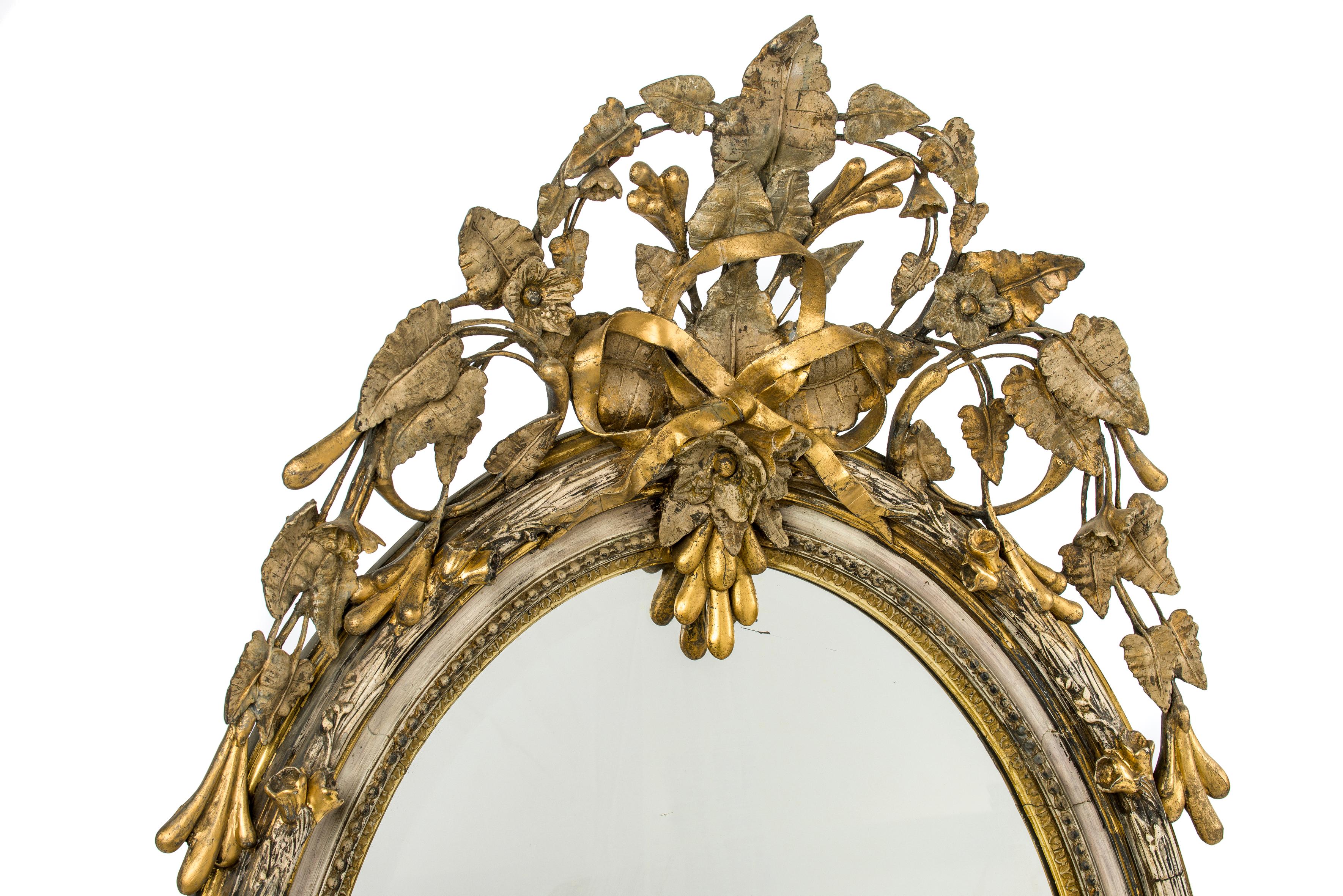 A beautiful and nature-inspired antique oval mirror that was made in France circa 1860. 
The most elevated part of the frame has a bark shape and is decorated with flowers and leaves. The frame is decorated with an intricate crest of the top and
