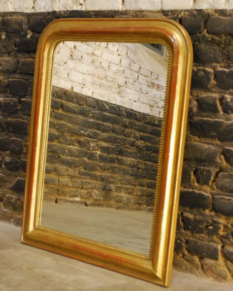 A beautiful small gold gilt Louis Philippe mirror made in France circa 1870. 
It has the upper rounded corners that are typical for a Louis Philippe mirror. The mirror frame is made in solid pine, smoothened with gesso and red earth. The red