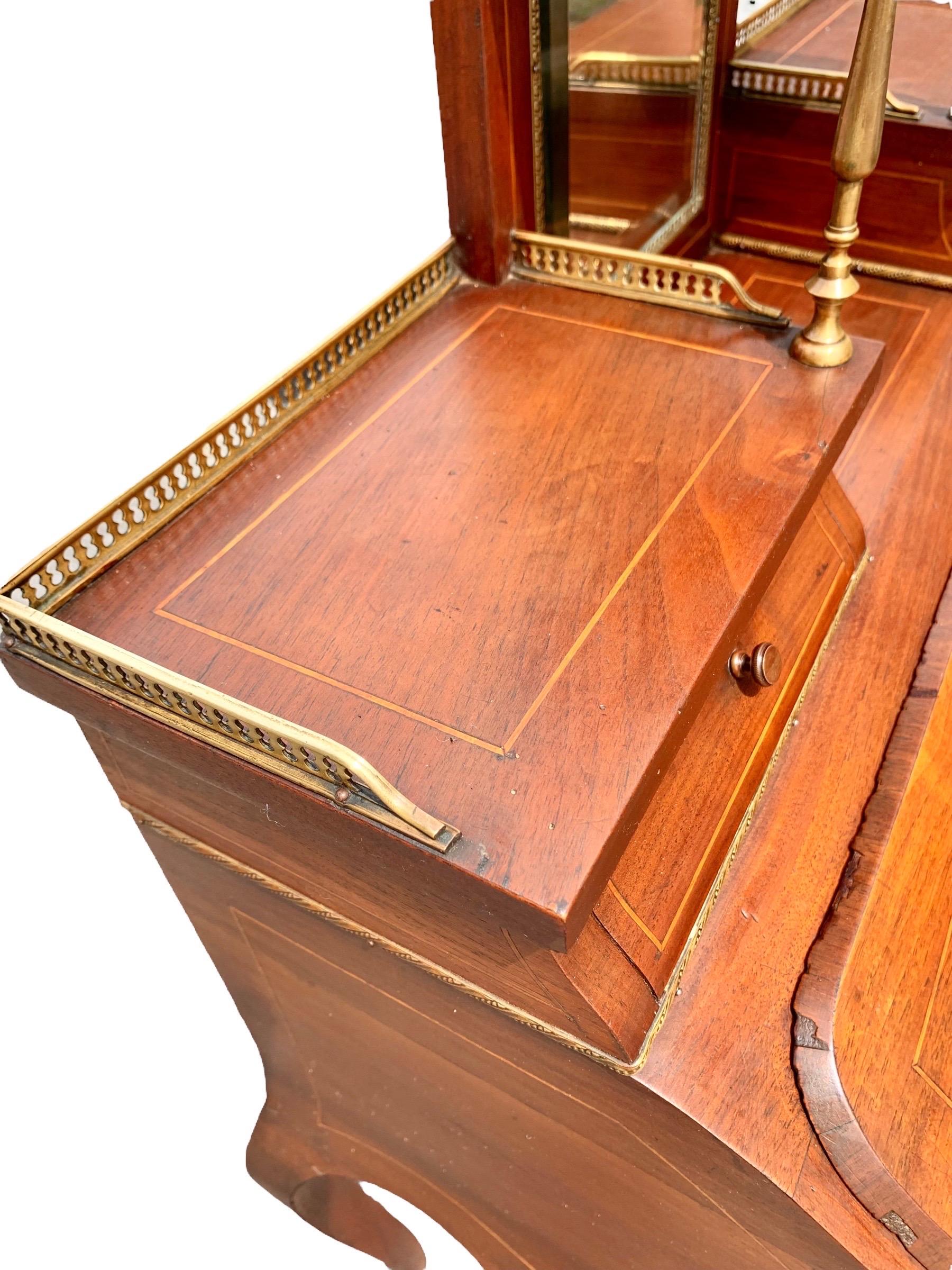 An antique French Louis XV style inlaid carved cherry Bonheur du Jour, 19th century with a raised brass galleried shelf above a wide beveled mirror back, flanked by two small brass galleried serpentine drawers over a marquetry inlaid slant front