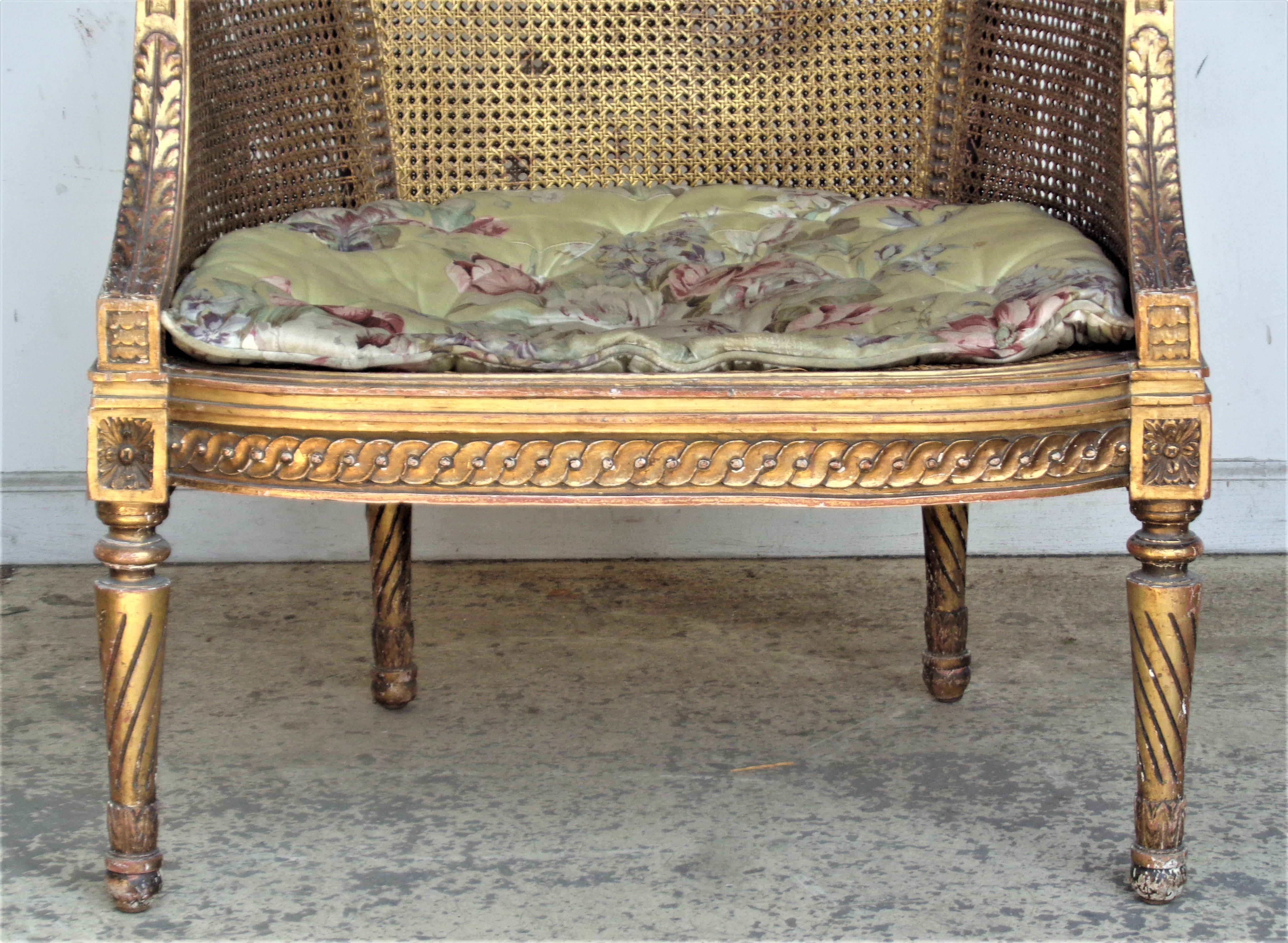Antique 19th century French Louis XVI style giltwood bergere with a finely carved frame in overall beautifully aged original gilded surface showing underlying areas of red bole highlights. The upper sides, back and seat with woven cane. Comes with