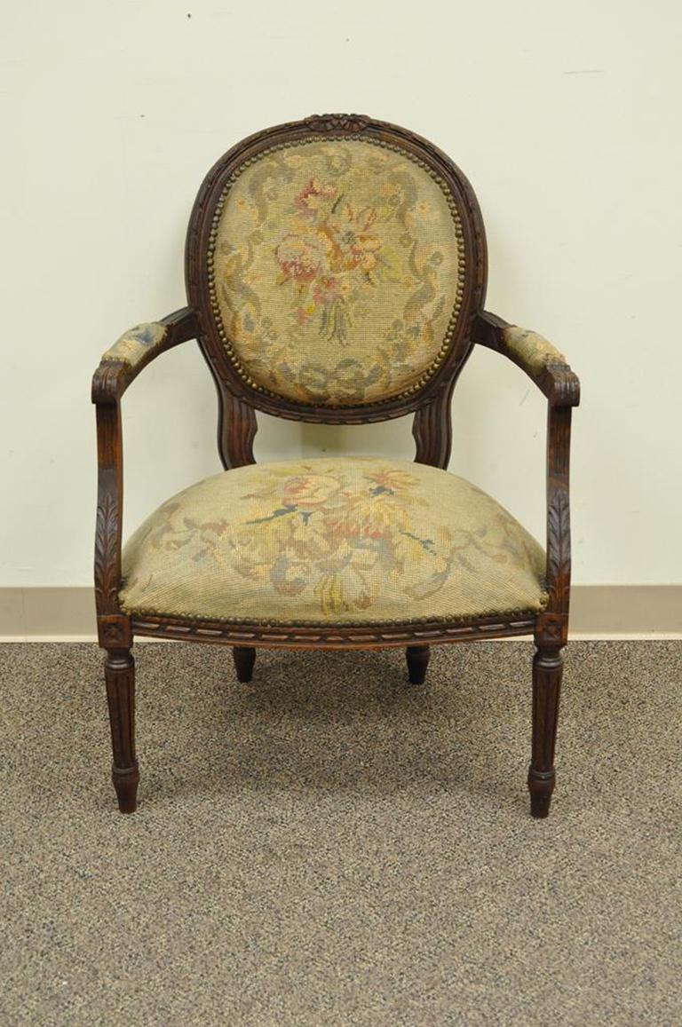 Antique 19th century French carved needlepoint armchair in the Louis XVI Taste. Item features original figural needlepoint upholstery, floral and ribbon carved walnut frame, reeded legs, and classic French form, circa mid-late 1800s, France.