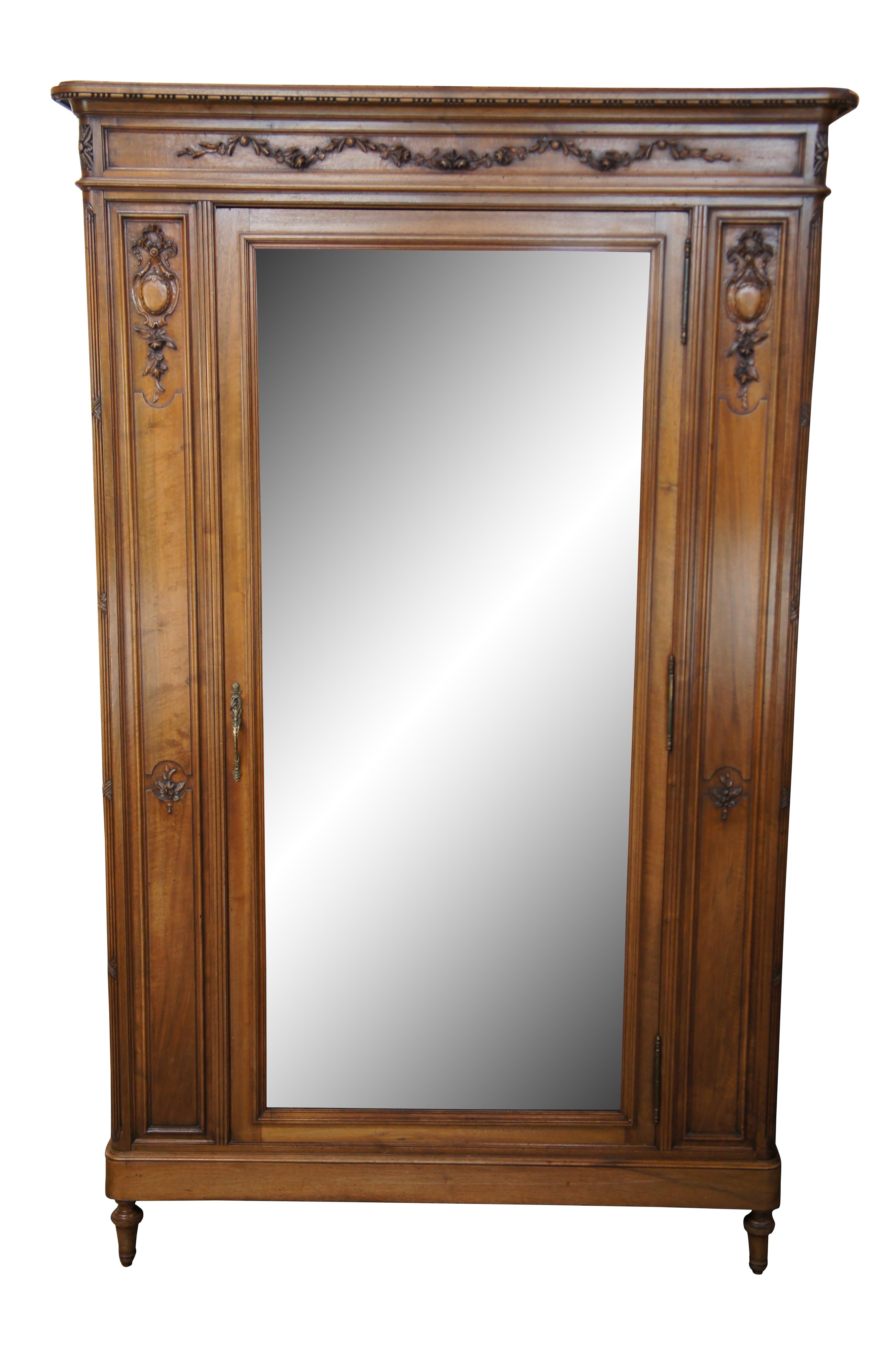 An extraordinary French Louis XVI knockdown armoire, circa 1870s. Made from walnut with a large central beveled looking glass / dressing mirror.   The case is carved in a classical manner with low relief foliate, neoclassical ribboned cartouches and