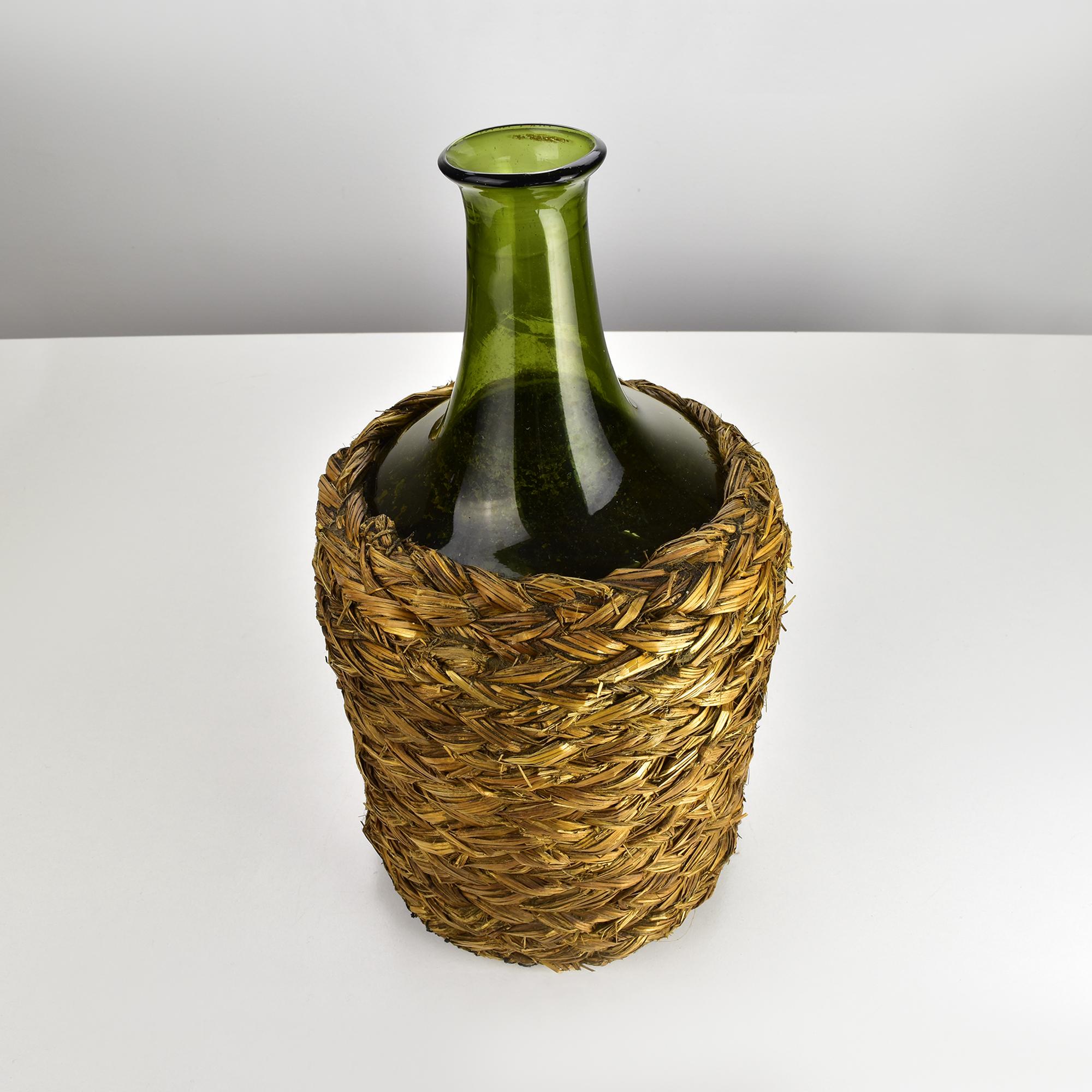 Esta damajuana antigua es una hermosa botella de vino de vidrio verde soplado, hecha a mano y con boca, que se guarda en una cesta de paja rústica. 

Esta pieza, que data de la segunda mitad del siglo XIX, es una verdadera antigüedad y un raro