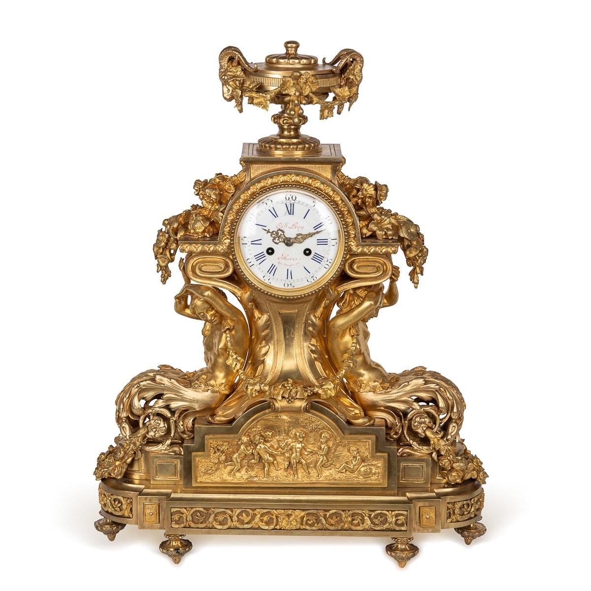 Antique 19th Century French garniture, cast bronze in ormolu, a striking ensemble featuring a pair of seven-light candelabras and a mantel clock. The clock is adorned with foliage and crowned with two regal ram heads, with the signature prominently