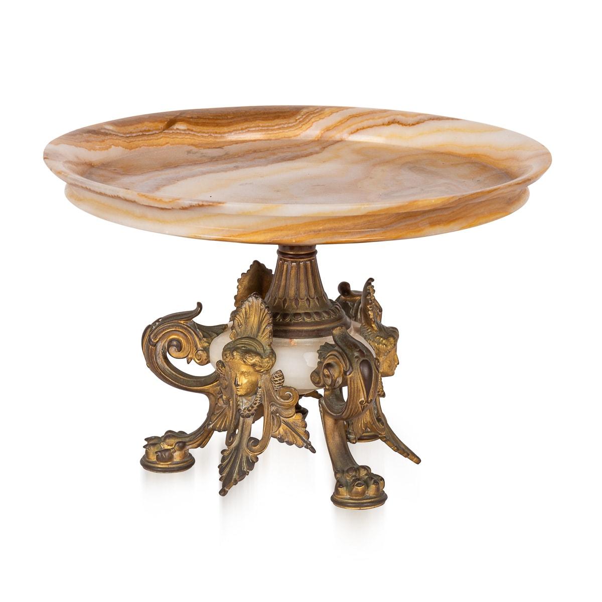 Antique magnificent 19th Century French ormolu mounted onyx marble tazza, masterfully crafted by Eugène Cornu, exudes timeless elegance. Resting upon a trio of exquisitely adorned ormolu-mounted legs, each embellished with leaf-capped scrolled