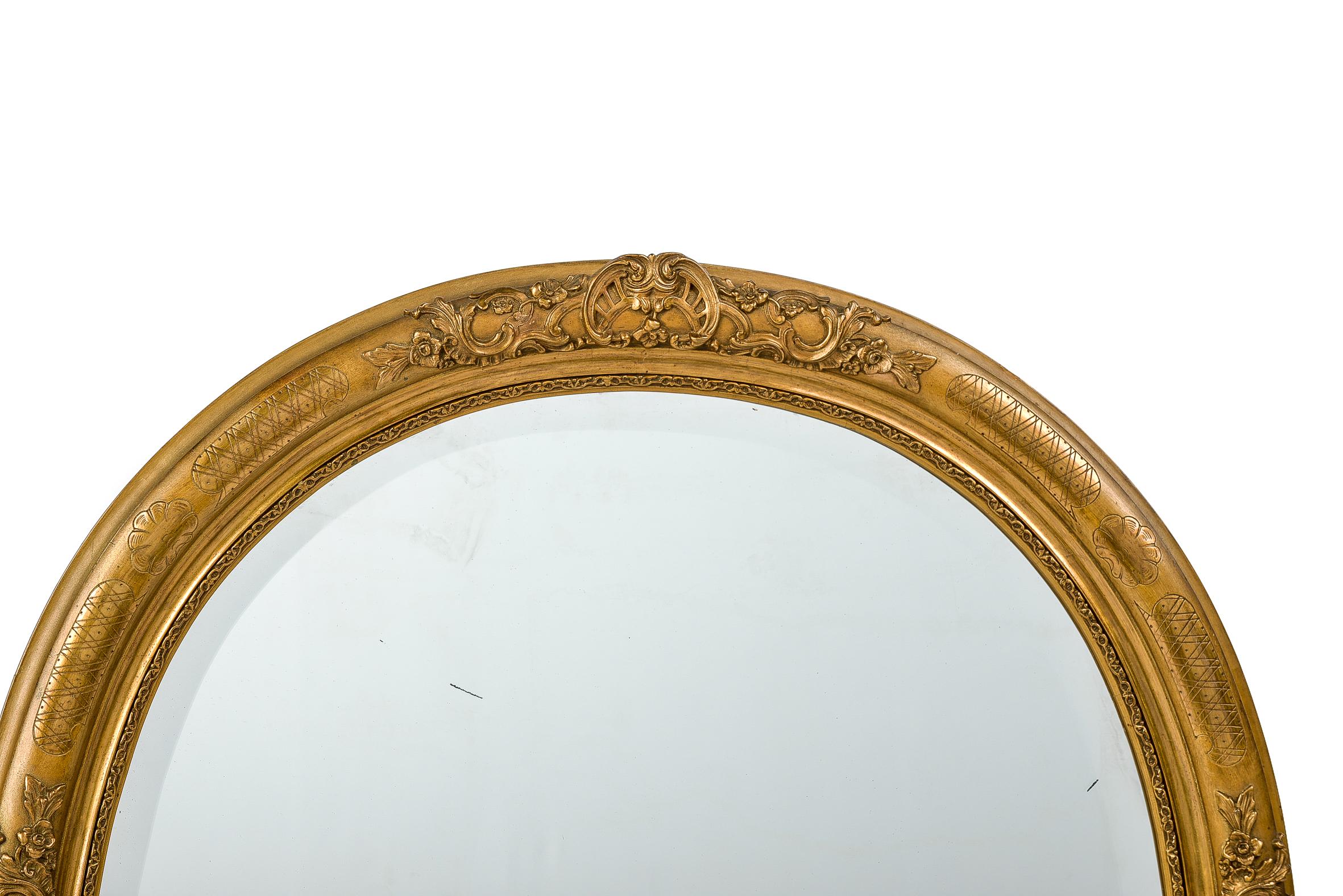 A beautiful antique French oval mirror that was made in France, circa 1890. 
The mirror frame is adorned with highly detailed ornaments that depict scrolls, acanthus, flowers, and leaves. 
The most elevated part of the frame has floral and cross