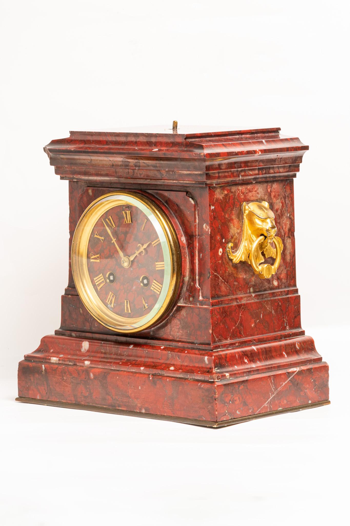 Antique 19th Century French Rouge Marble Mantle Clock made by well known French clockmaker Japy Frères circa 1890. This rouge veined marble and ormolu mounted two train clock is decorated with bronze lion heads on each side holding ring handles in