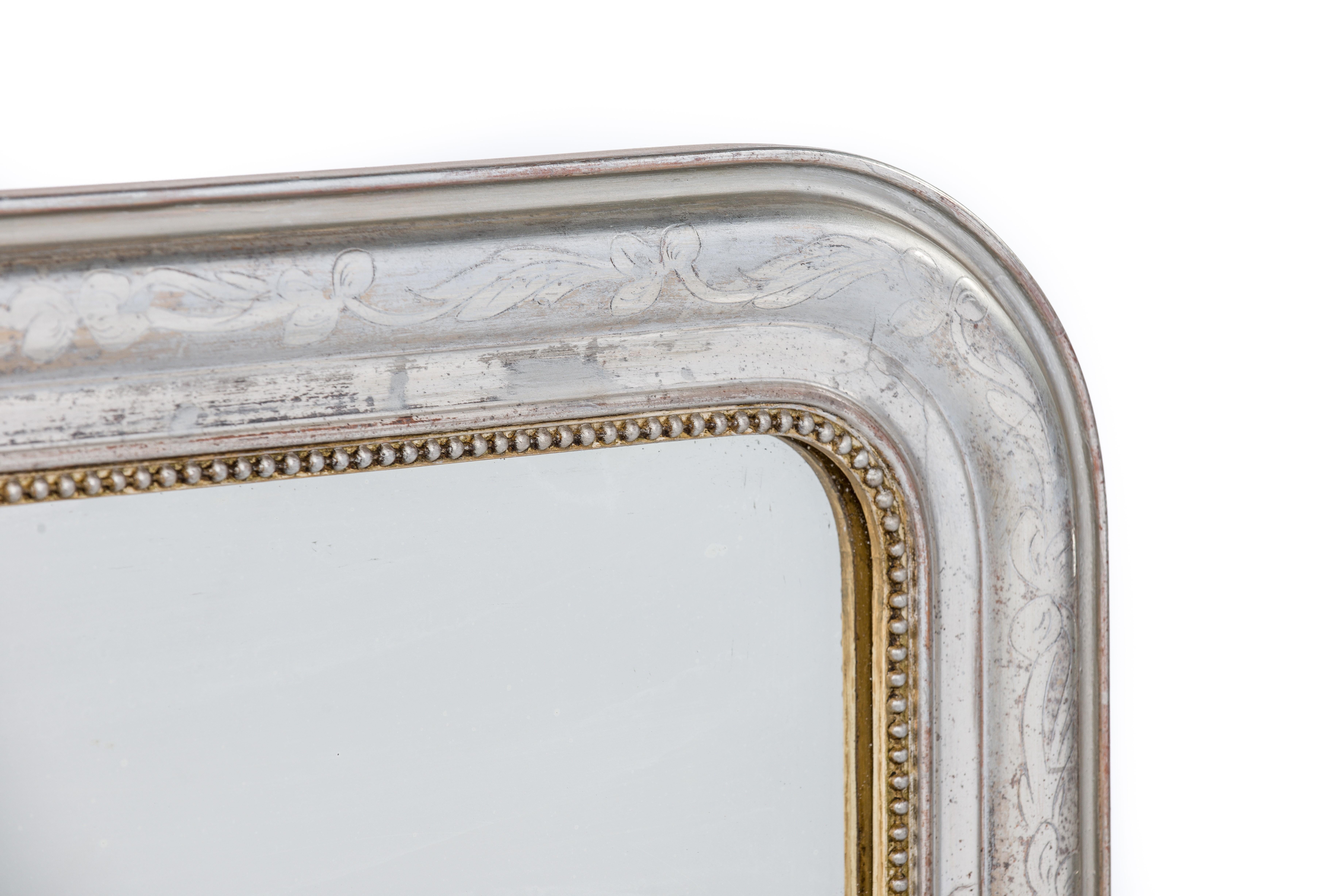 This is a beautiful completely silver leaf gilt Louis Philippe mirror. It features the upper rounded corners typical for Louis Philippe mirrors. The frame is decorated with a floral engraving on the most elevated part of the frame. A pearl beading