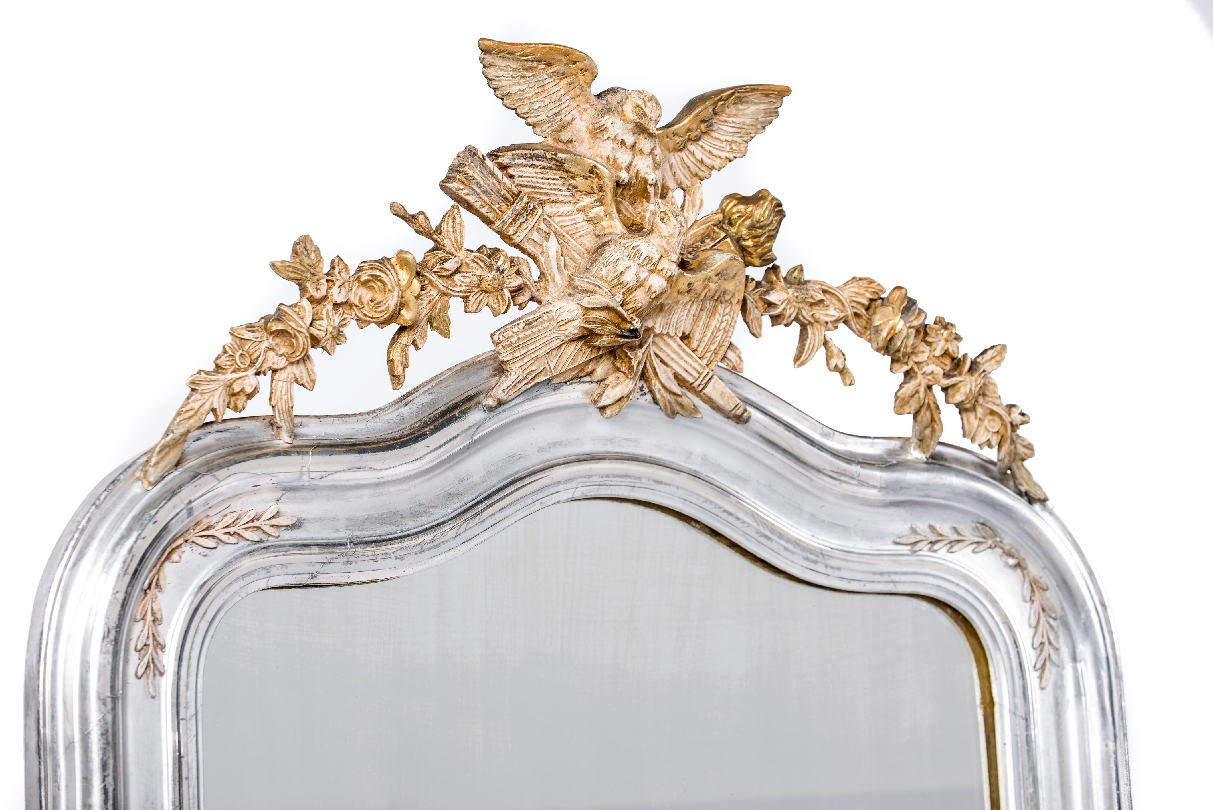 This unique mirror was made in Northern France at the end of the 19th century. The mirror frame has the upper rounded corners typical for the Louis Philippe style. The mirror features a serpentine shaped top enriched with an ornate crest. The crest