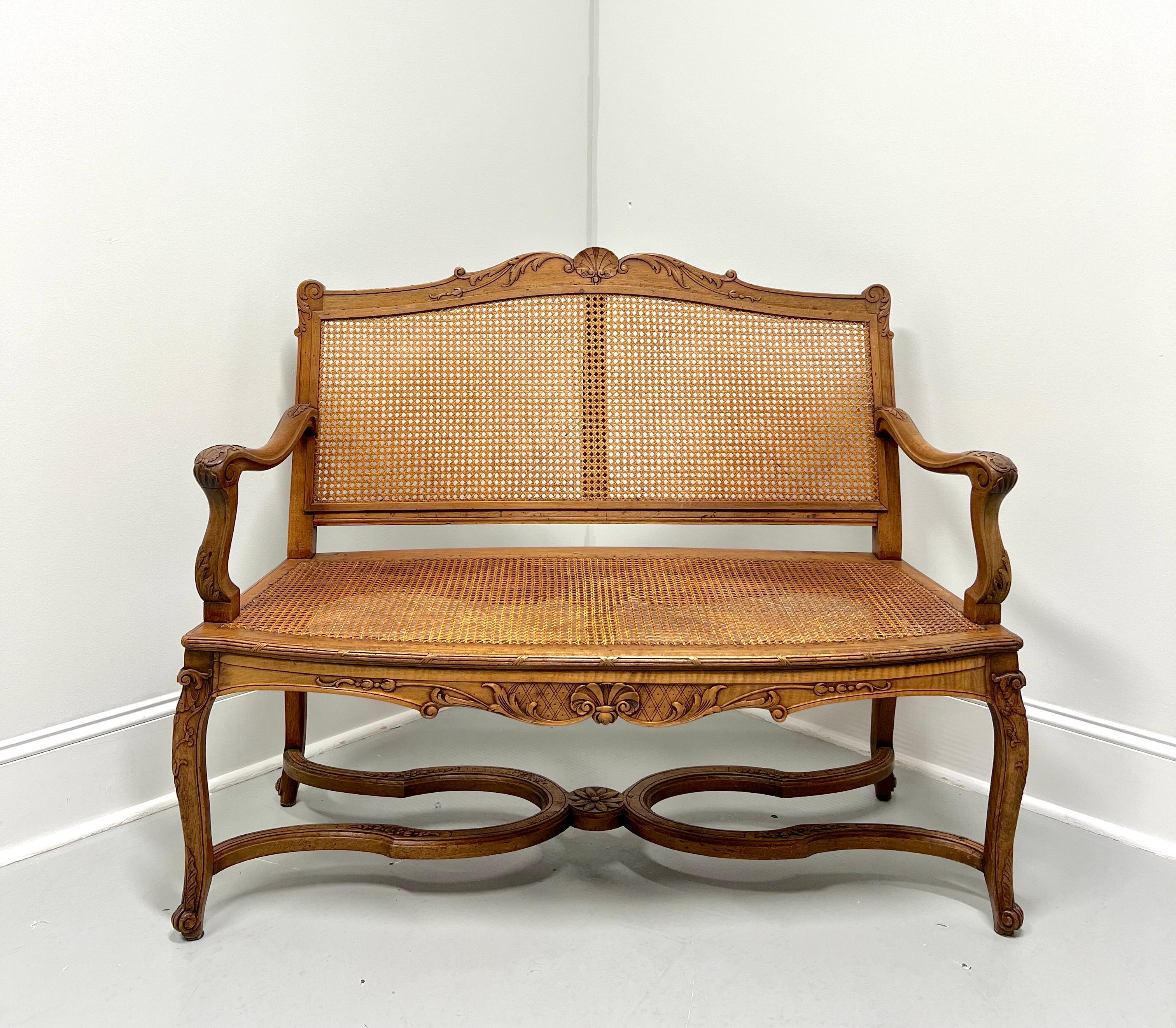 An antique French Provincial Louis XV style caned settee, unbranded. Solid fruitwood with decoratively carved crestrail, caning to the back, curved carved arms with carved supports, caning to the seat, carved apron & knees, dual carved U-shaped