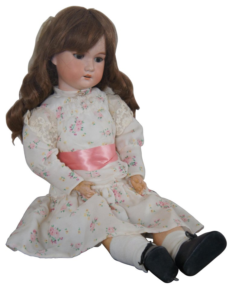 Antique German bisque head doll by CM Bergmann with articulated jointed limbs and composite body, non-original human hair, sleep eyes, marked “Made in Germany CM Bergmann II” on back of neck, dressed in a floral dress with pink sash and
