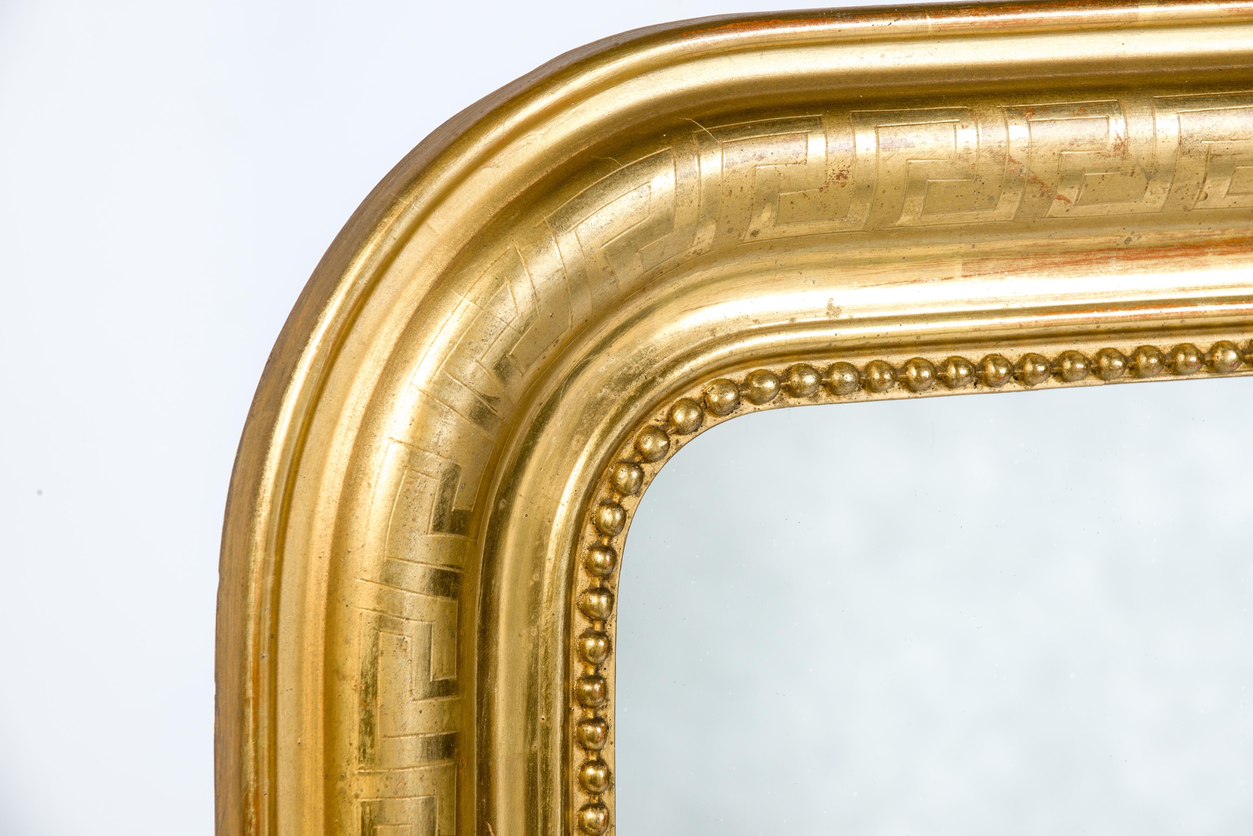 A beautiful gold leaf gilt French mirror. It has the upper rounded corners typical for the Louis Philippe style. The mirror frame has an elegant pearl beading surrounding the glass. The most elevated part Is engraved with a Classic geometric Greek