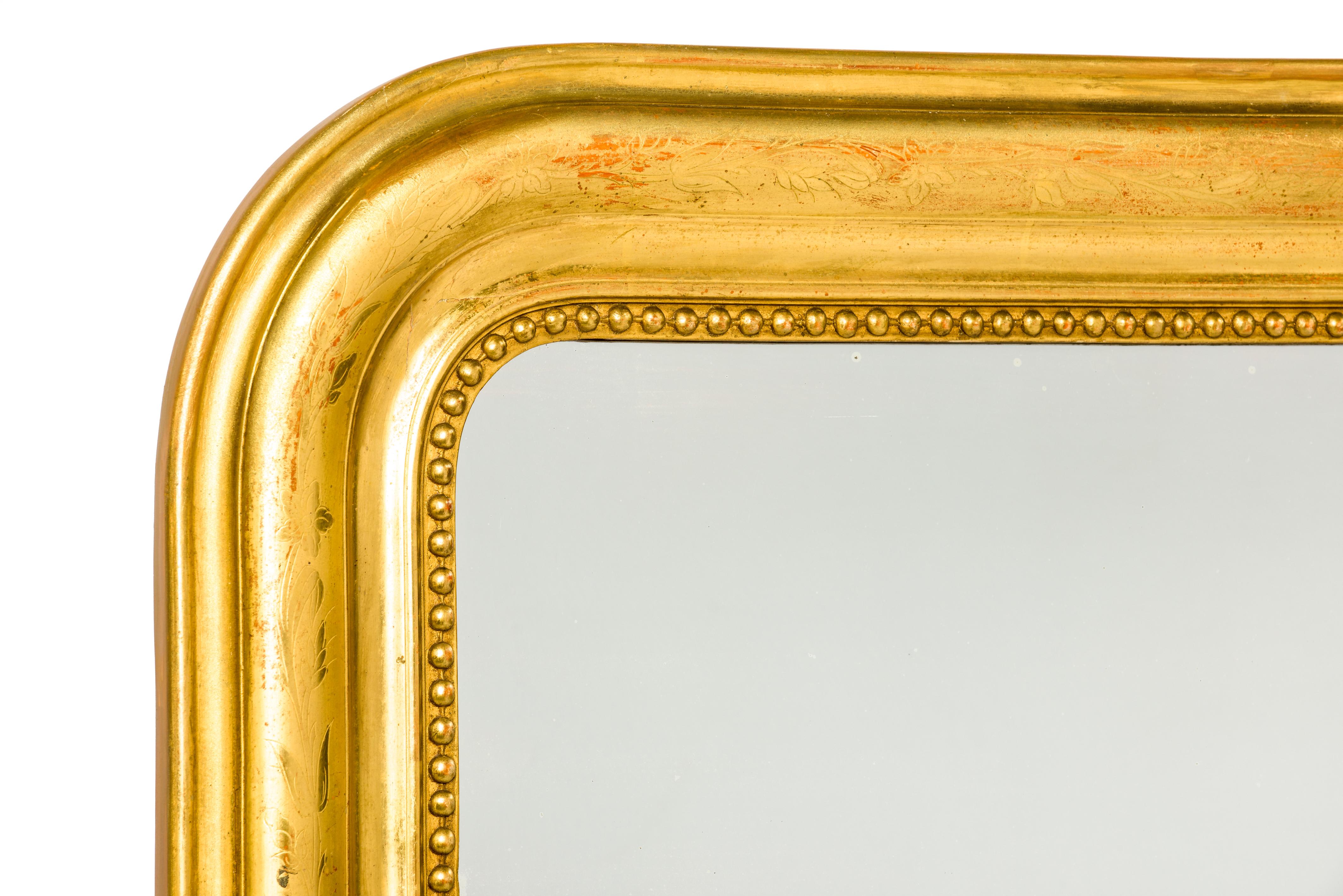 This beautiful and tall antique French mirror is completely gold leaf gilt and is made in Louis Philippe style with it's typical rounded upper corners. The mirror frame has a classic pearl beading surrounding the glass. The most elevated part of the