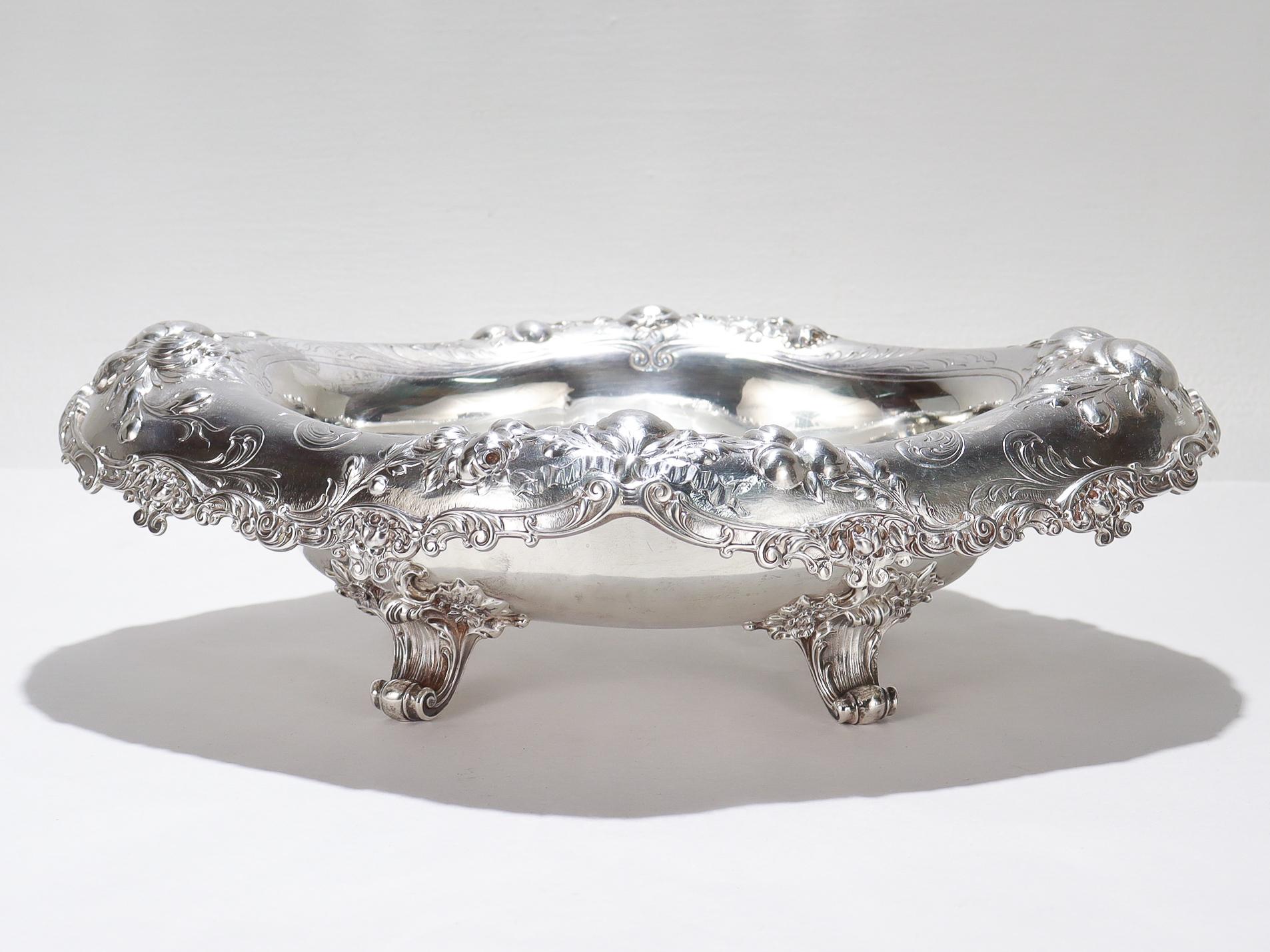 Una bella fruttiera antica o un centrotavola.

Da Gorham. 

In argento sterling.

Risale al 1896.

Con un ampio bordo martellato a mano, con frutta e fiori in repousse, una sezione di ciotola ovale lobata e quattro piedi a voluta pesante. 

La base