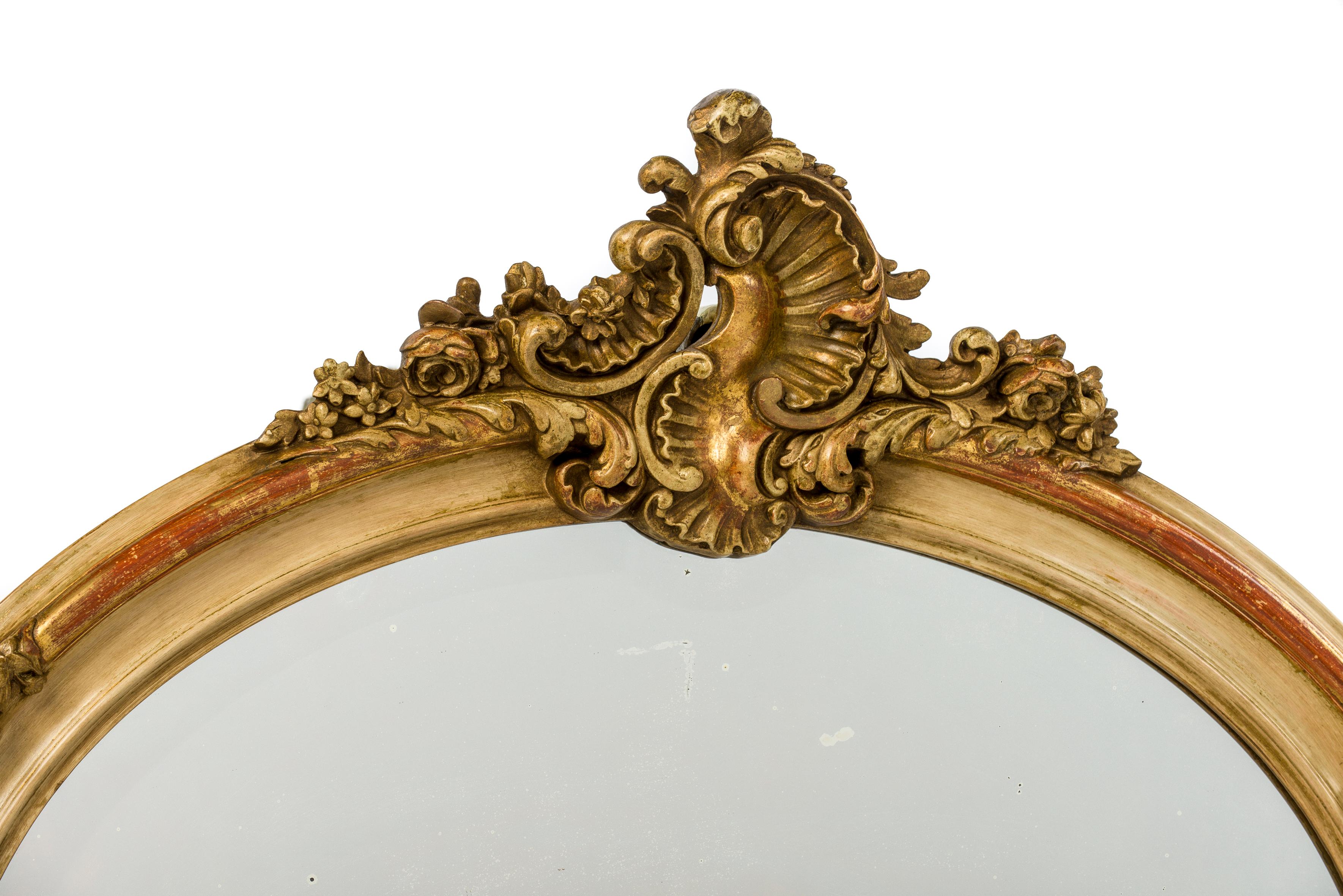 This is an elegant oval mirror that was made in France in the late 1800s. The mirror frame is beautifully decorated with asymmetrical ornaments typical for the Louis Quinze style. The top ornament has a central shell motif flanked by C scrolls,