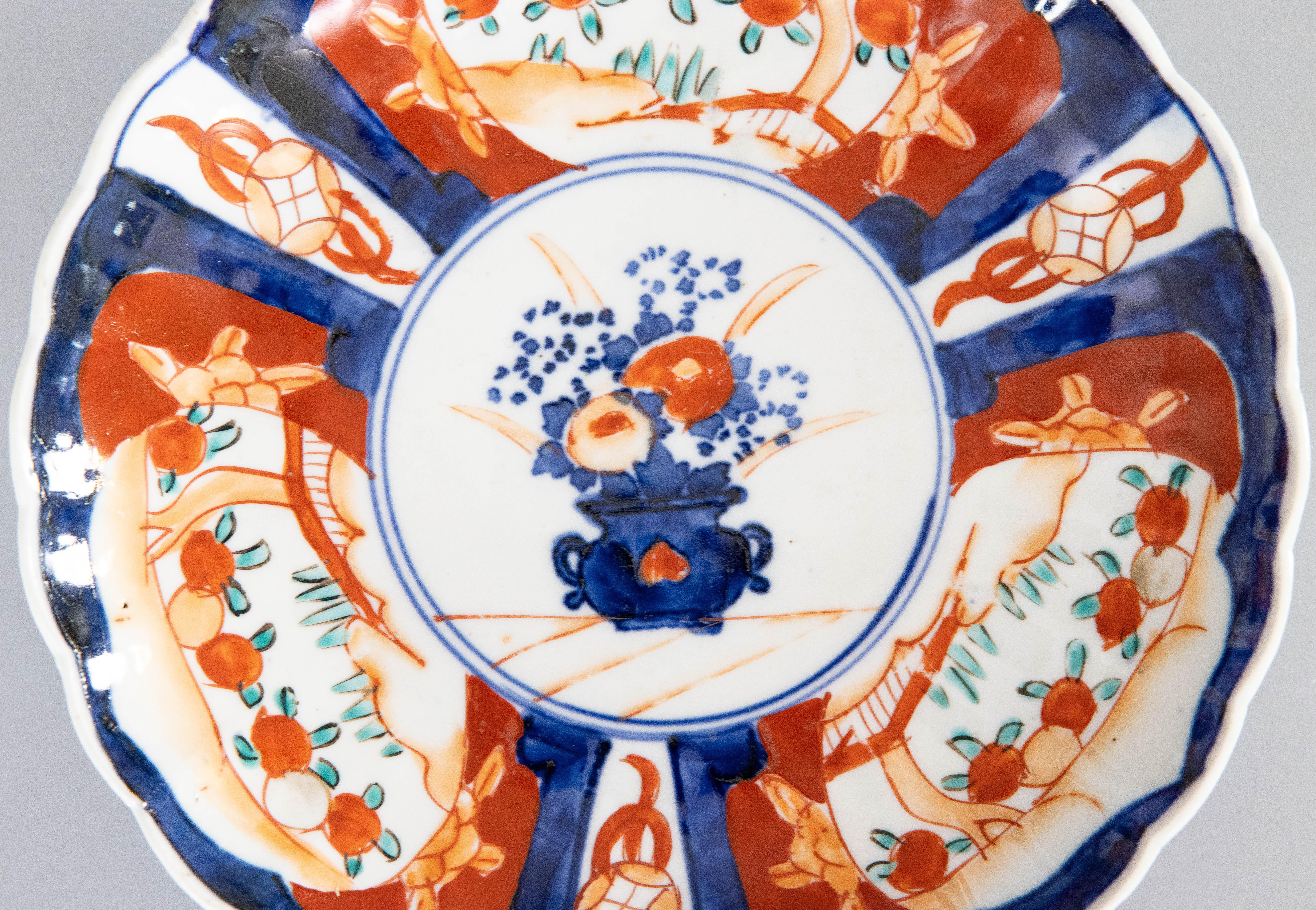 Wonderful 19th century antique Imari plate with scalloped edge. Featuring vibrant oranges, blues, and green. The center of the plate depicts a hand-painted vase with a spray of flowers. 