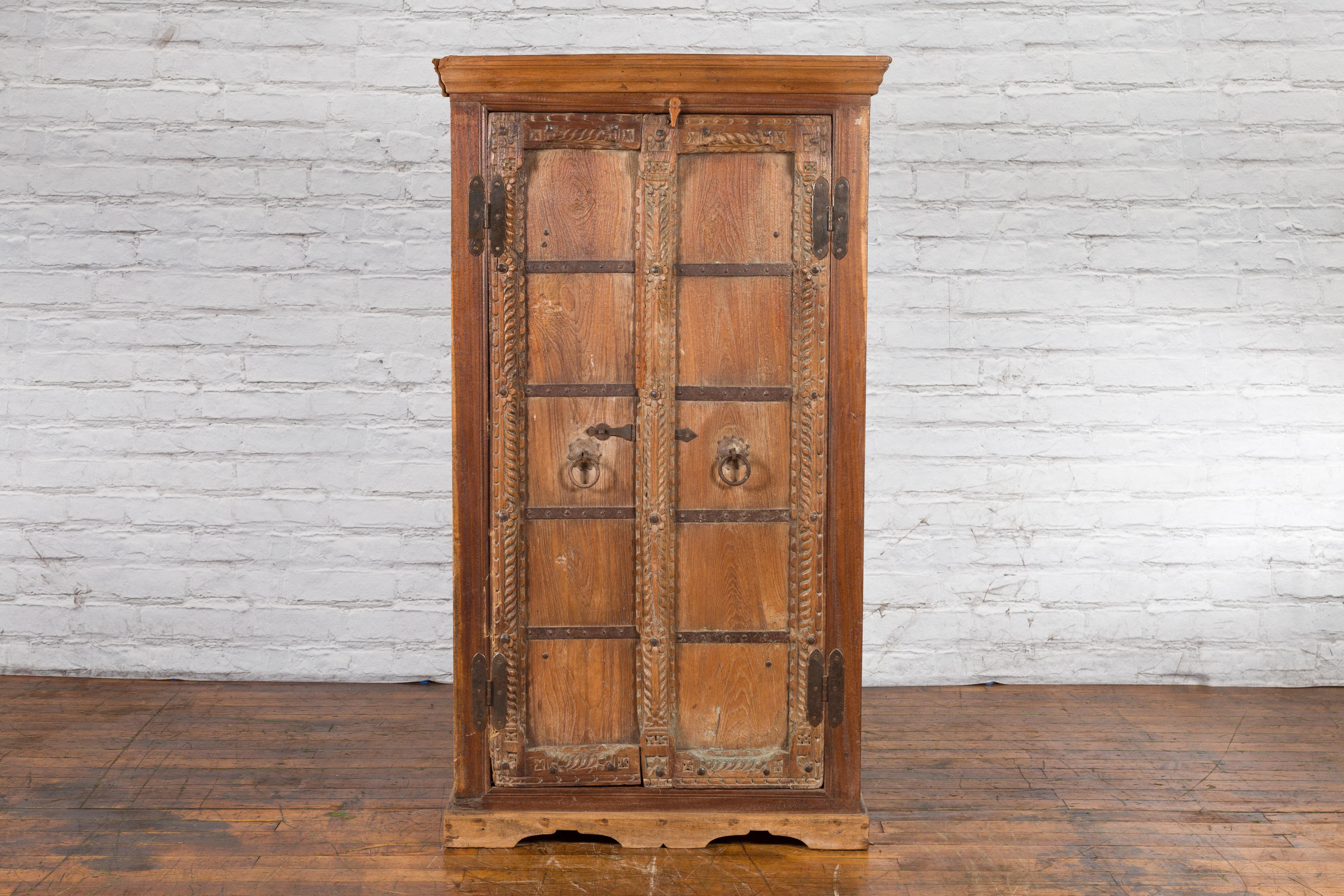 An antique Indian hand-carved wooden armoire from the 19th century with metal braces, twisted molding and floral carvings. Created in India during the 19th century, this wooden armoire features a molded cornice sitting above a set of double doors,