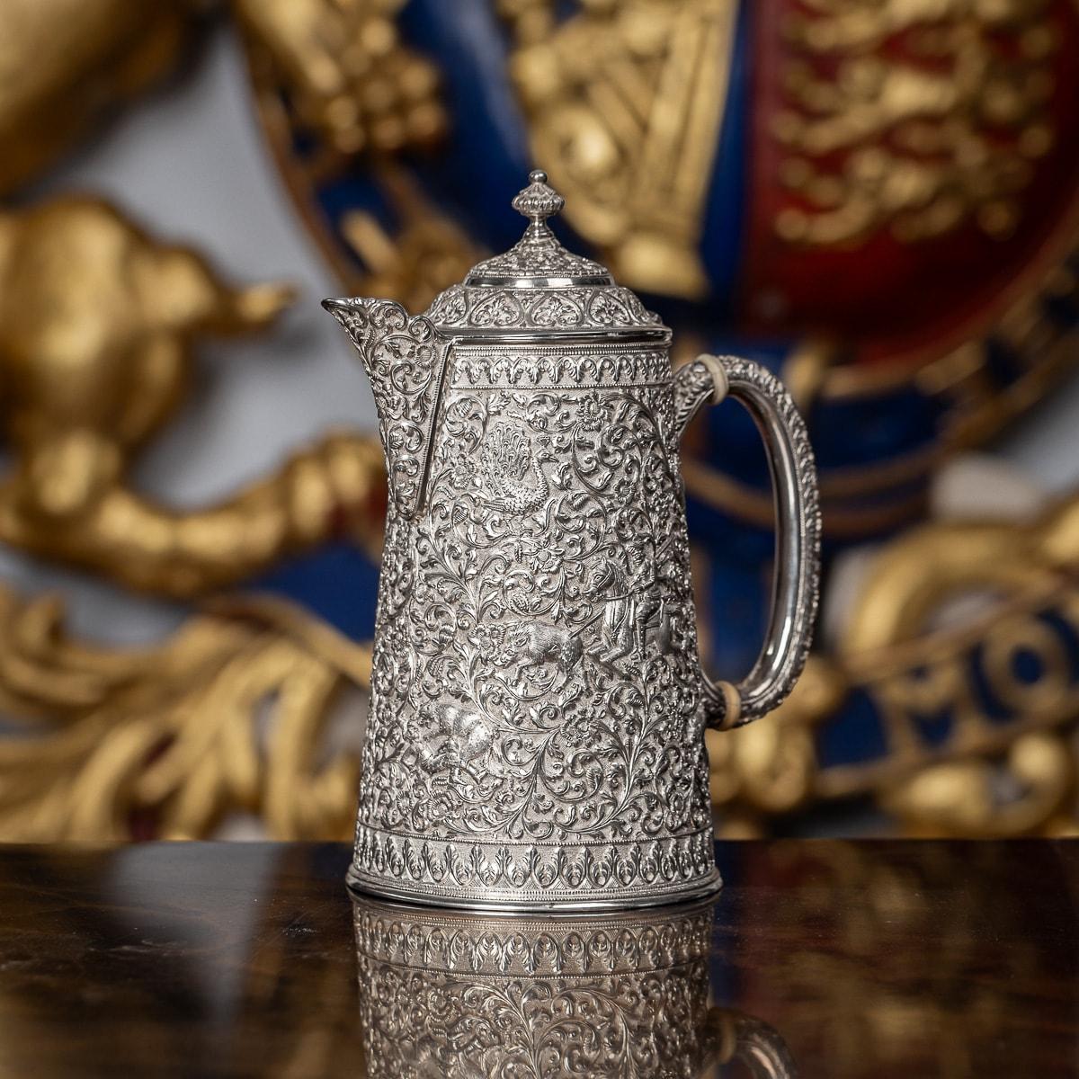 Antique 19th Century Indian Colonial solid silver ewer, straight body resting on a circular base, c-shape handle and hinged lid surmounted by a knob and ball finial. The piece is profusely and intricatly chased with scrolling leaves, flowers and