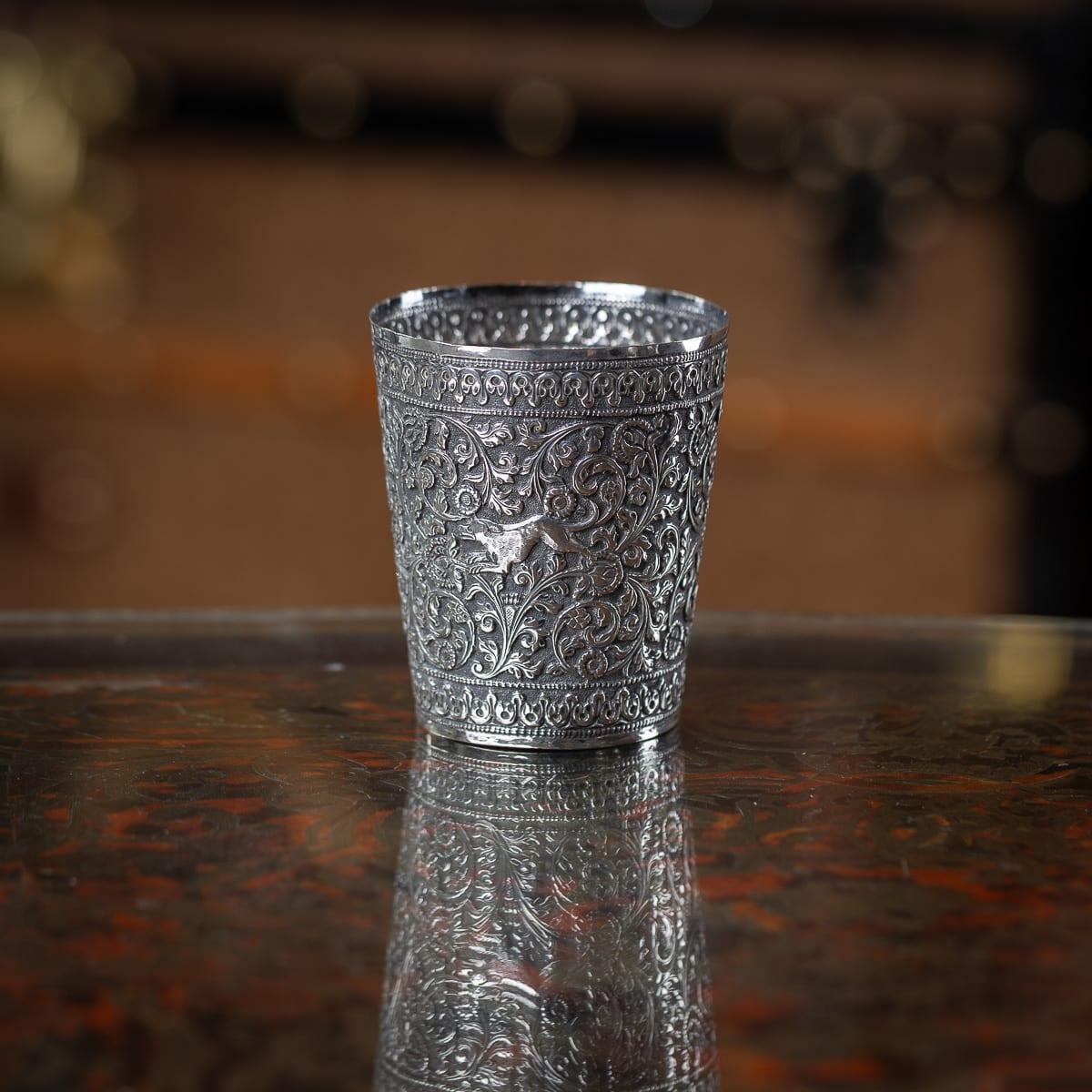 Antiguo vaso de plata maciza de la India (Kutch) del siglo XIX, de forma cónica con intrincadas volutas de hojas, flores y hojas de acanto sobre fondo mate. Alrededor del vaso hay representados varios animales, en el típico estilo kutch (cutch). No