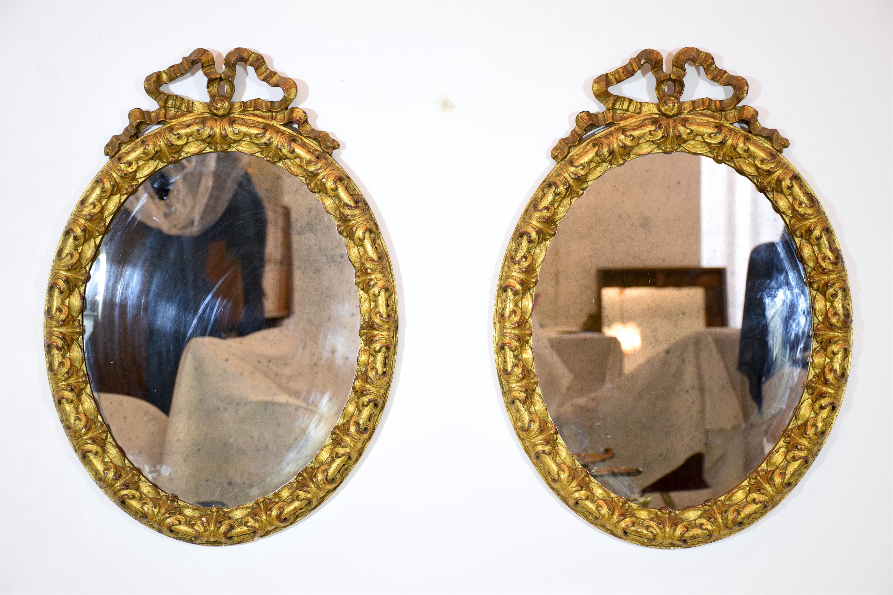 Pair of antique Italian oval vanity boudoir giltwood wall mirrors with ribbon shaped ornaments at the top in Rococo style. Italy, late 19th century. 
All original pieces.
The glass can be replaced as an additional request. 


 