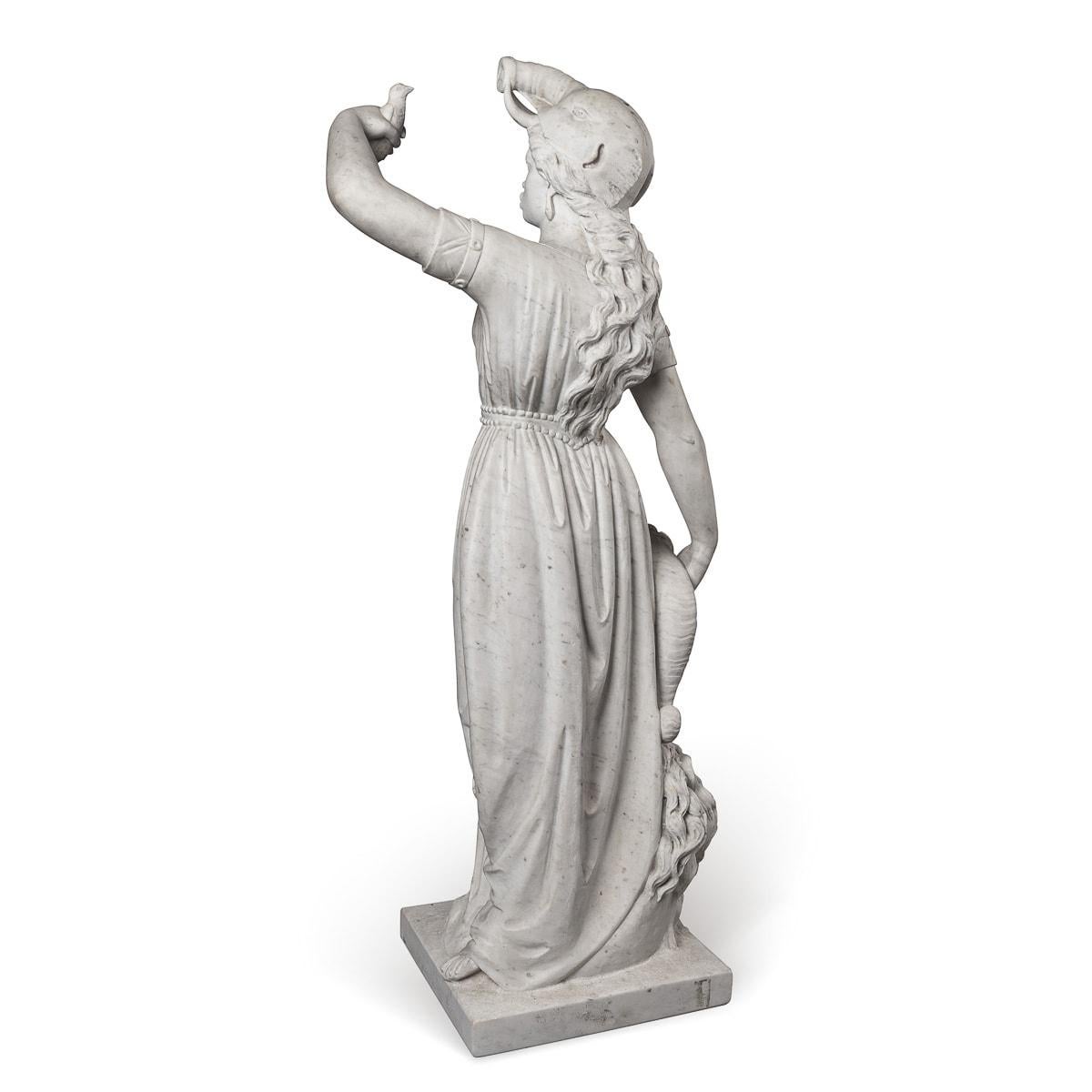 Crafted in the mid-19th century, this antique Italian marble sculpture portrays a graceful African lady draped in robes. Crowned with an elephant head, she delicately holds up a small bird in one hand, while the other hand rests beside her leg,