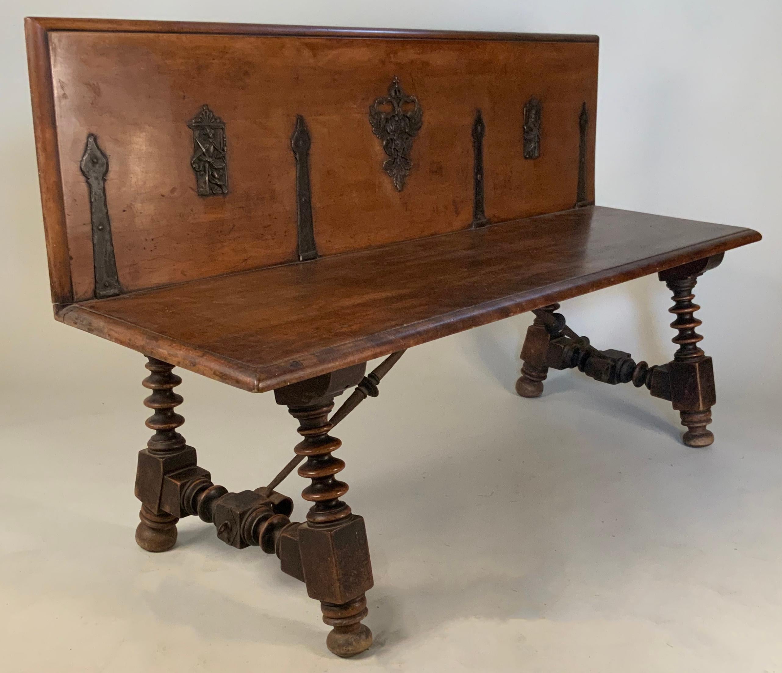 A very unique antique late 19th century Italian walnut bench, with a back likely made from a repurposed trunk lid. The base of elaborately turned spindle legs, connected with iron fittings and stretchers. The back retains the original iron hinge