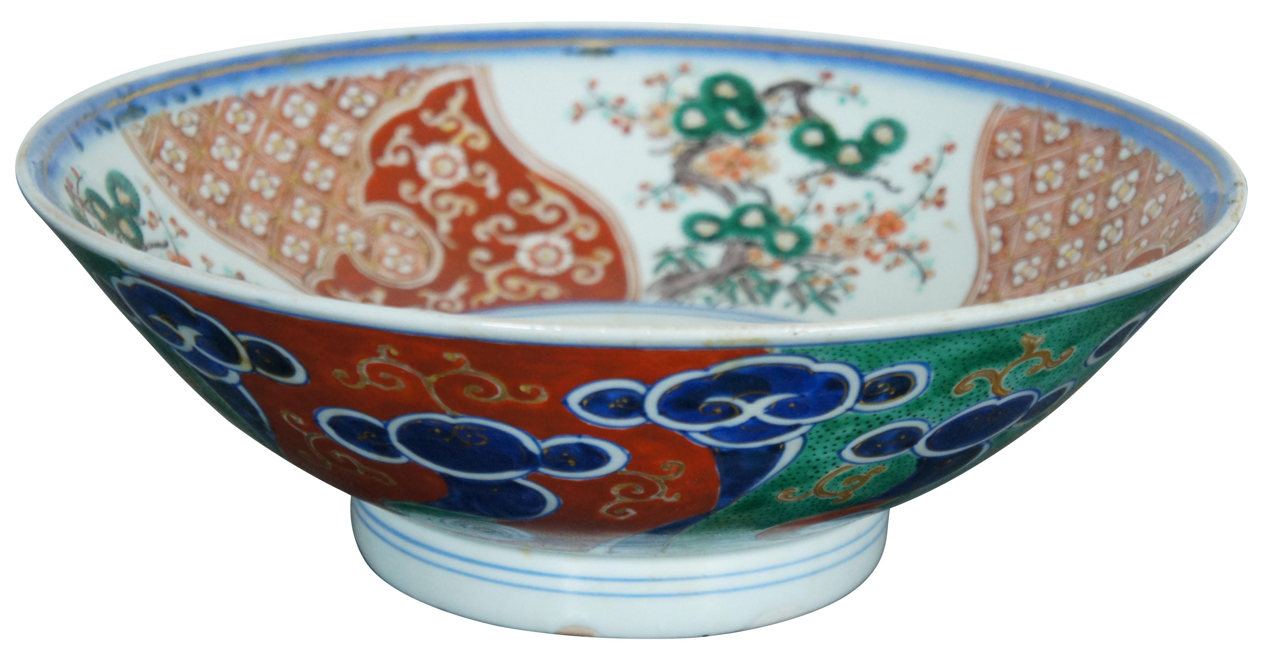 Antique Japanese Meiji period porcelain polychrome footed serving or centerpiece bowl, decorated with red and white florals, gnarled pines, and swirling clouds.