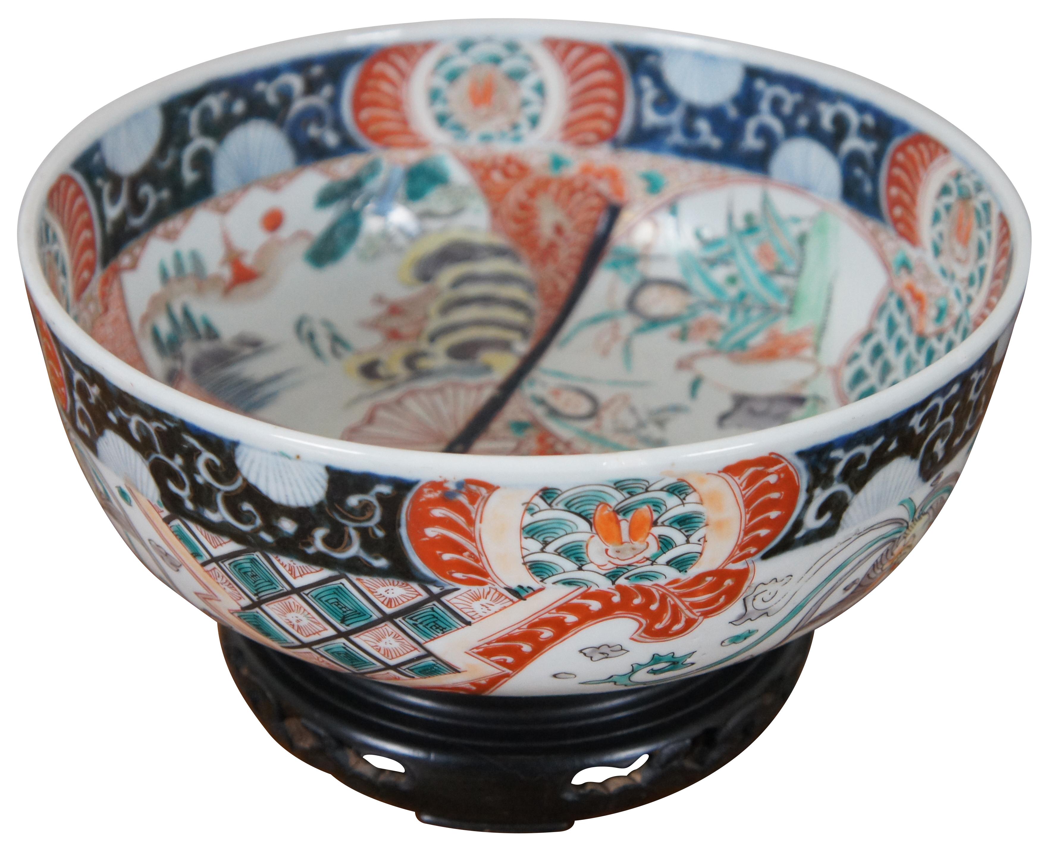 Antique hand painted 19th century Japanese Imari bowl decorated in orange and blue with phoenixes flying around the exterior. The interior features doubled images of a small penguins or chicks / birds in a pagoda garden and folding fans decorated