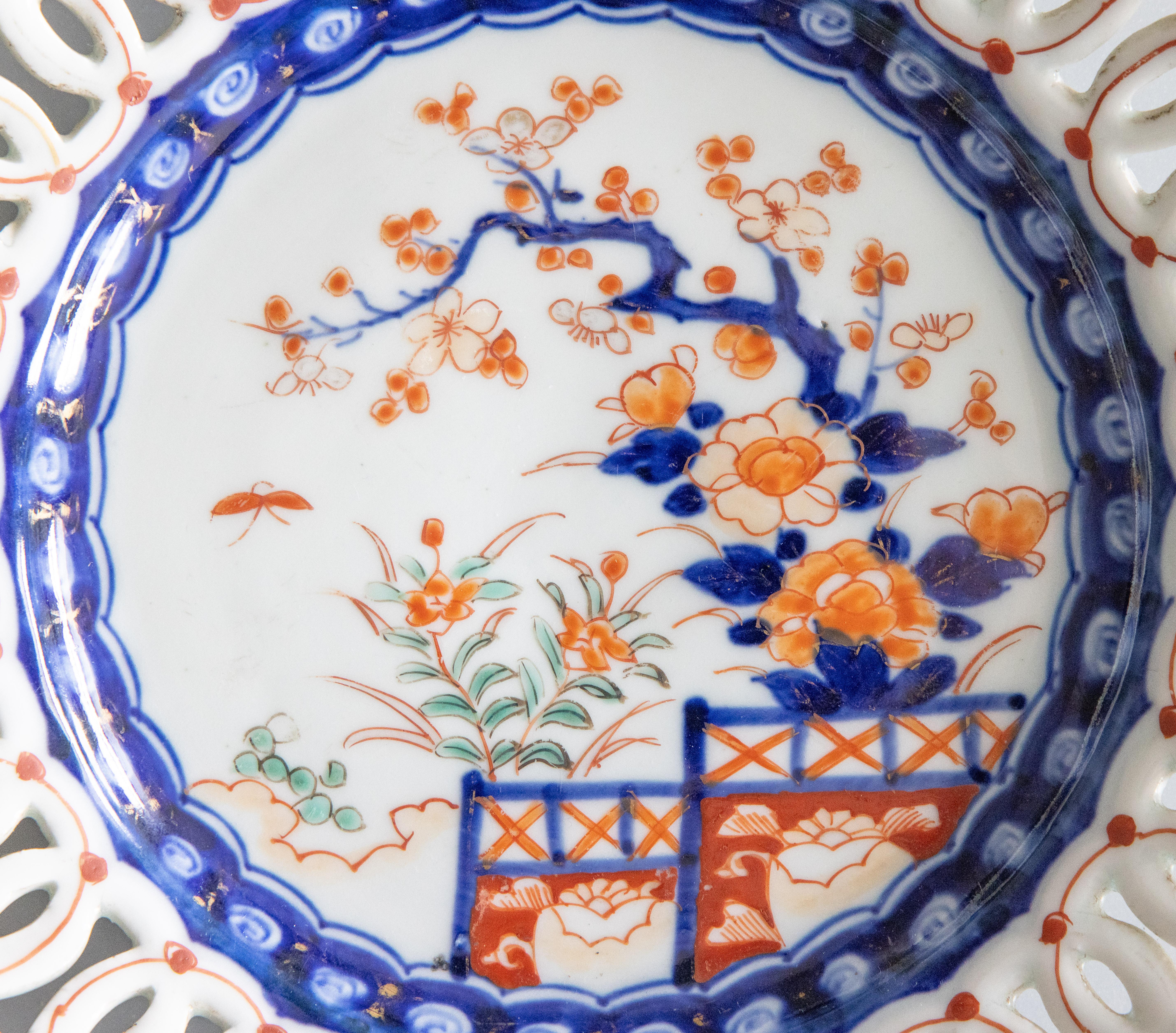 A wonderful 19th century antique Imari plate with a reticulated edge. Featuring vibrant oranges, blues, and green. The center of the plate depicts a hand-painted spray of flowers and garden gates.
