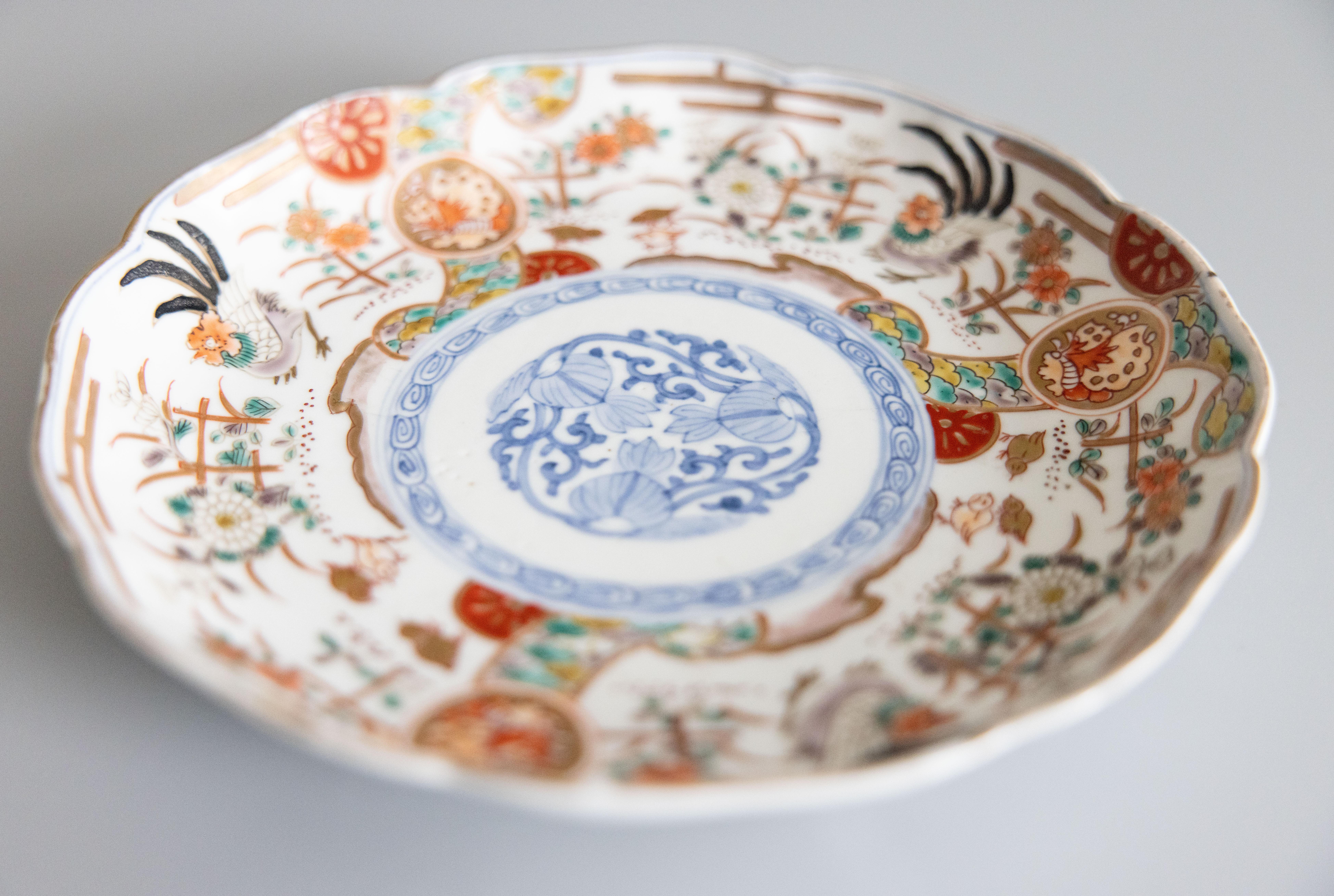 A striking 19th century antique Imari plate with a scalloped edge. Featuring vibrant oranges, blues, and green. The multi-color design depicts traditional Japanese motifs, showcasing the intricate craftsmanship of the era. The border features