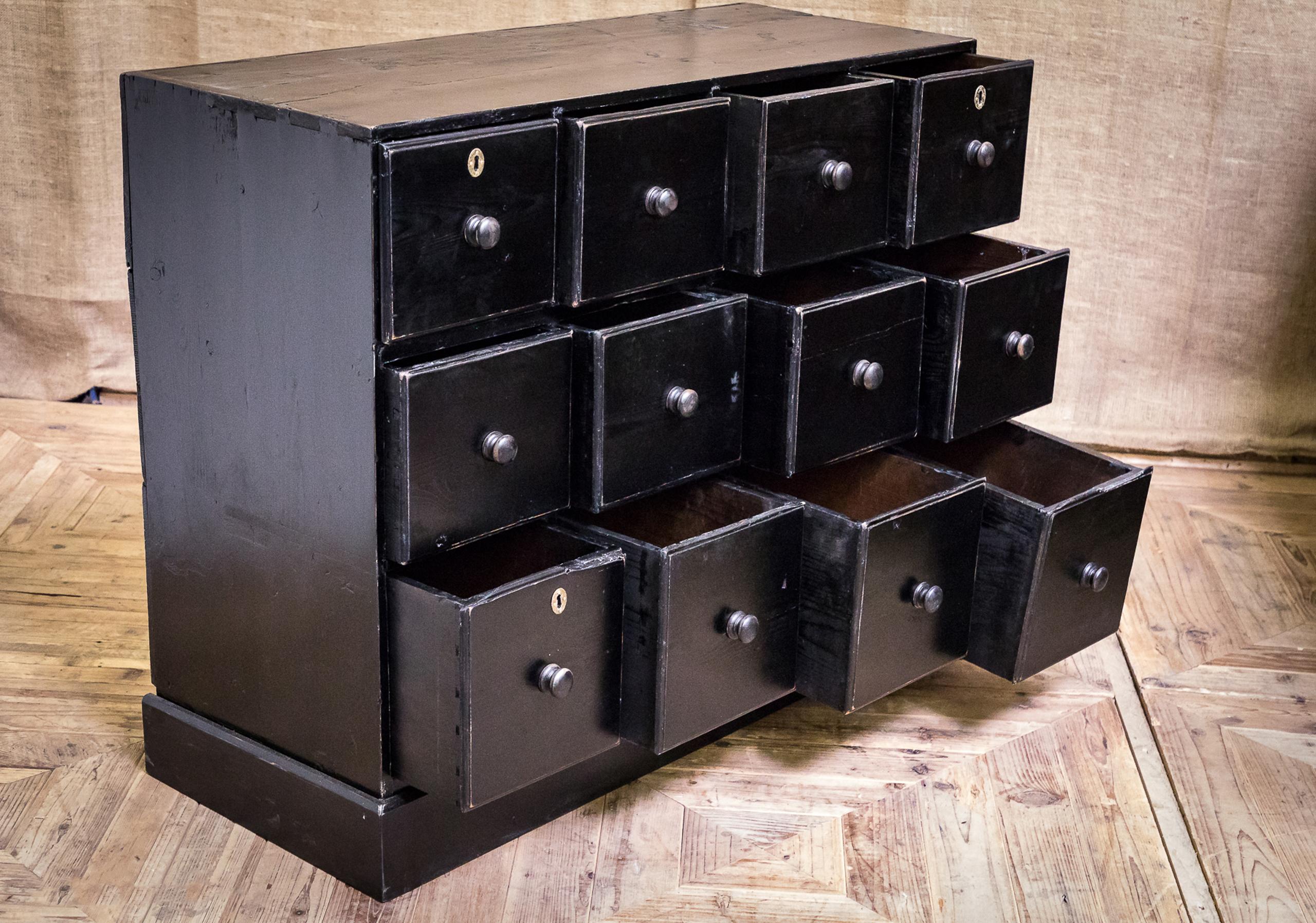 A wonderful large-scale bank of twelve apothecary drawers. Constructed of pine with an ebonized finish and turned handles to the drawers.
    