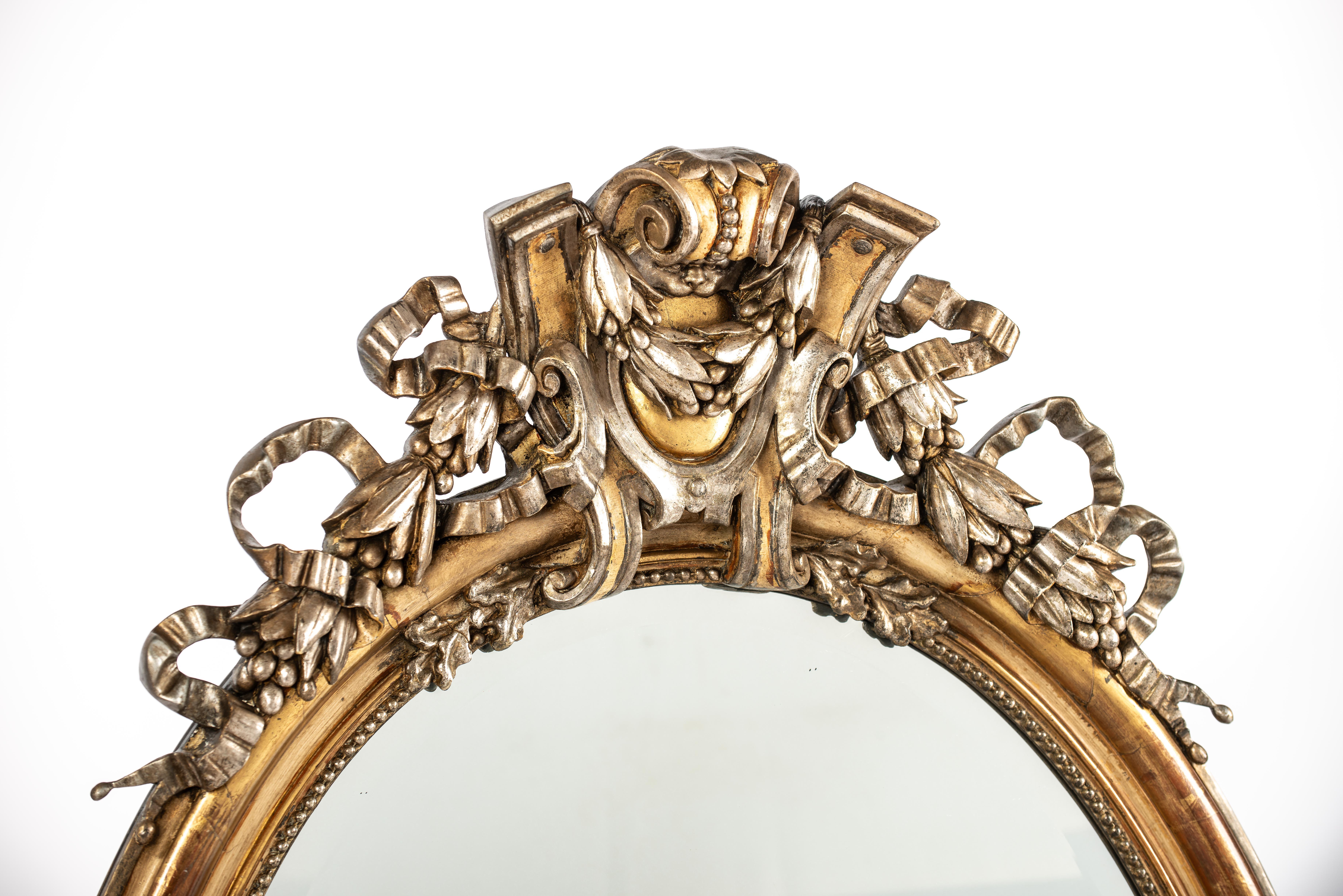 On offer here is a large antique oval mirror that was made in France in the second half of the 19th century, circa 1860. The mirror is decorated with beautiful ornaments with rich symbolic meaning. 
The top ornament on the mirror features a