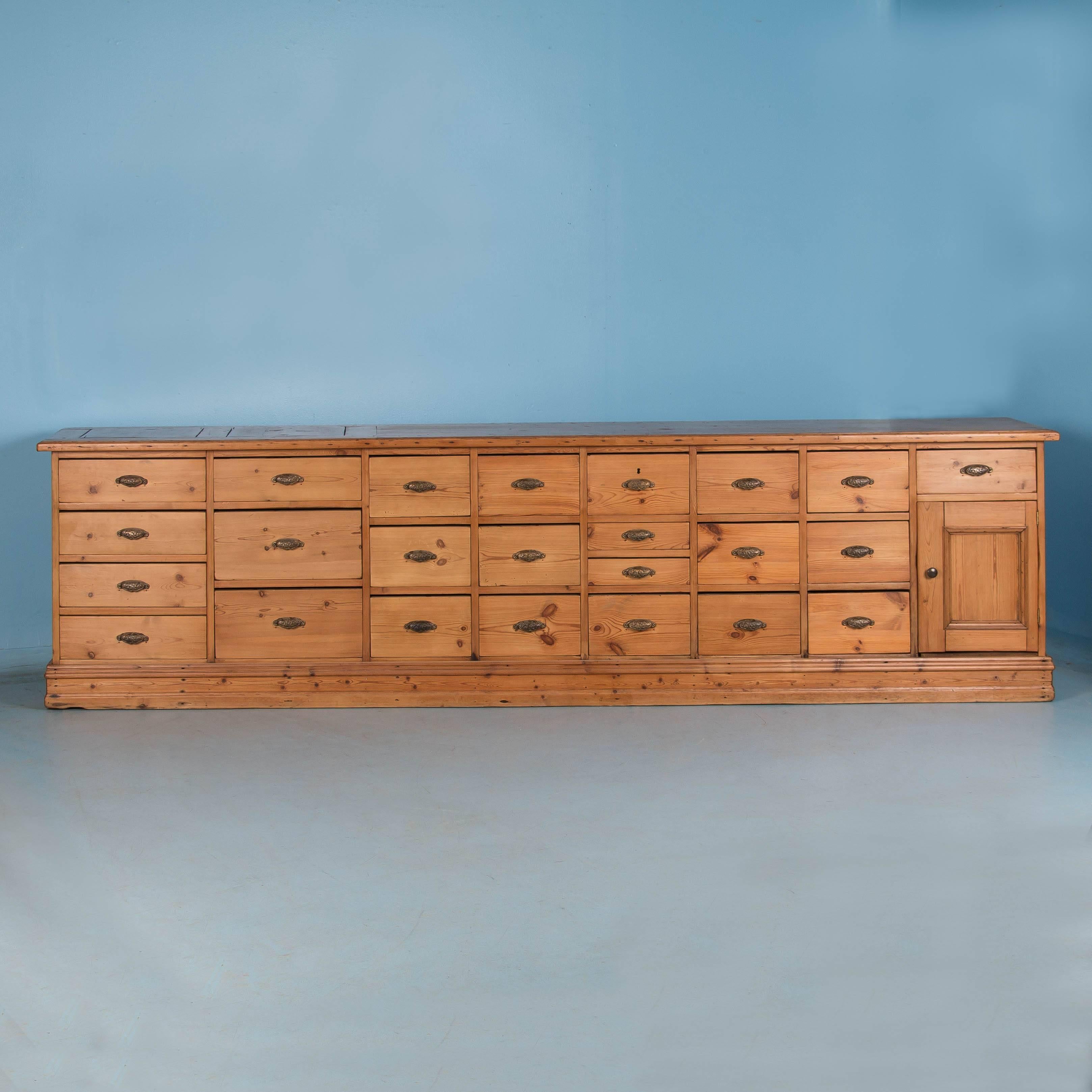 This long and very unusual antique pine grocer's cabinet from Denmark, was purpose built with 24 drawers in a variety of sizes and originally served as shop counter in the mid-1800s. The sides and back are finished with panelling, allowing this