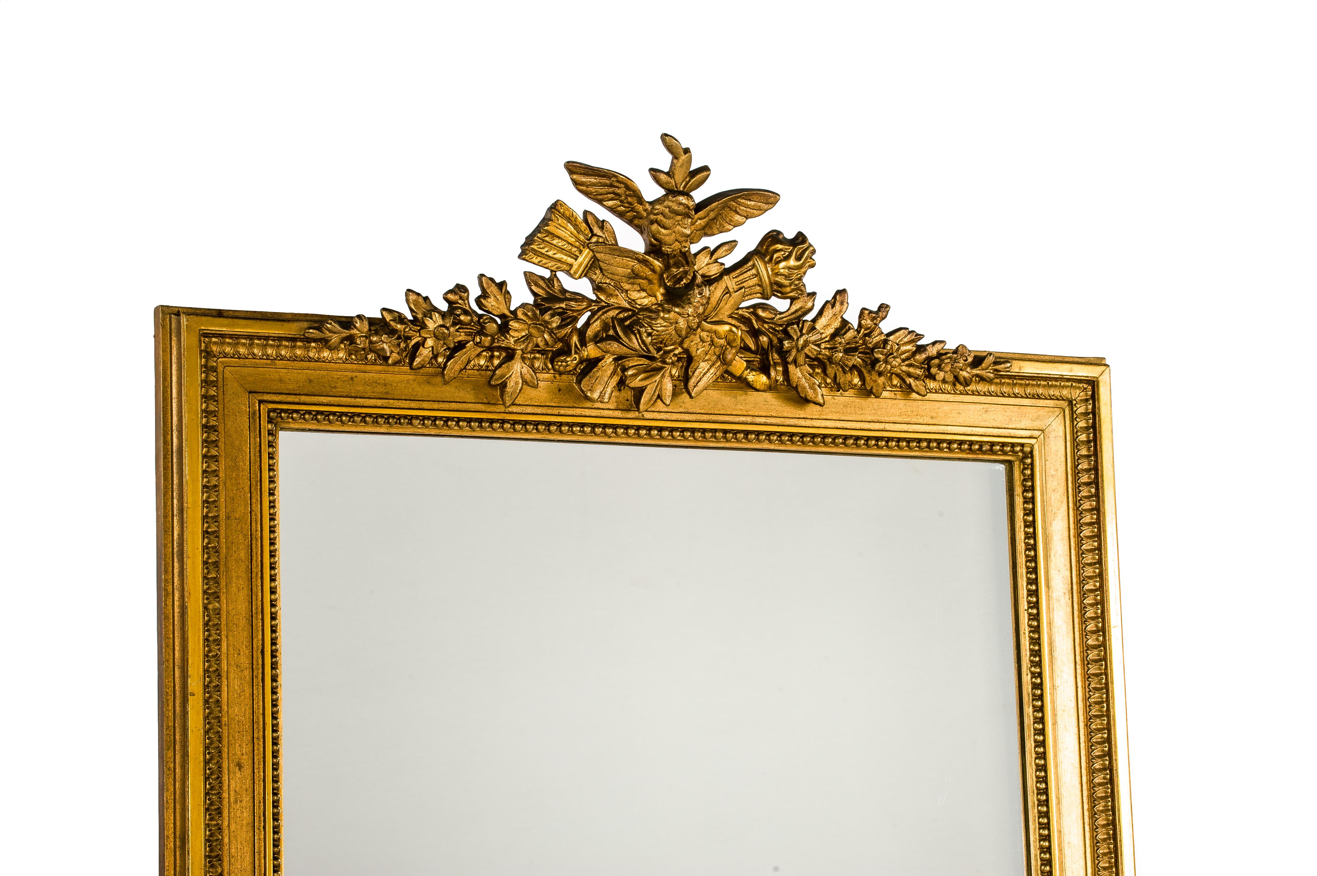 A very handsome and tall pier mirror that was made in the late 19th century in Northern France. 
Its square frame, stylized laurel, and crest are typical for the Louis Seize style. The elaborate crest features a central crossed torch and arrow with