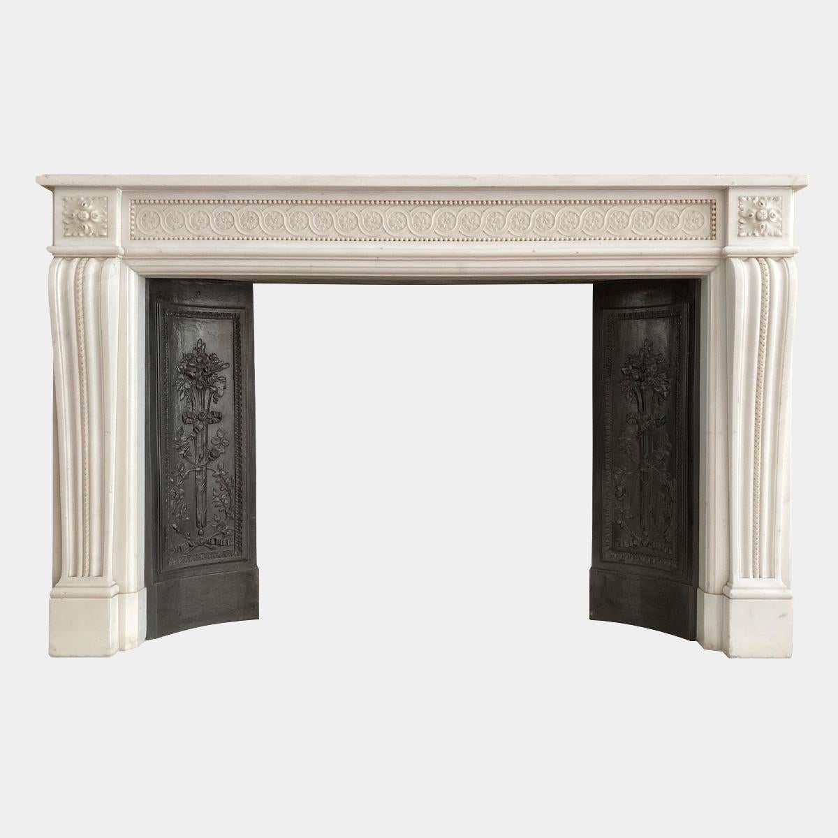 A large superior quality statuary white marble French fireplace surround in the Louis XVI style. The tapering console jambs with scaled carving within deep fluted mouldings, surmounted by square Patarae corner blocks. The beaded frieze having carved