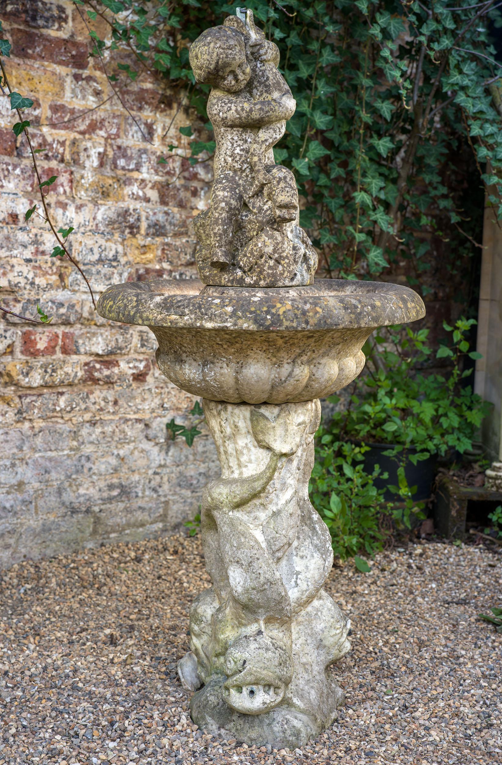 An antique marble fountain in the Baroque style, with a tripartite dolphin base each with a water spout in their mouths, their tails supporting the generous lobed bowl, which is topped a putto clutching a dolphin, designed to be seen through the