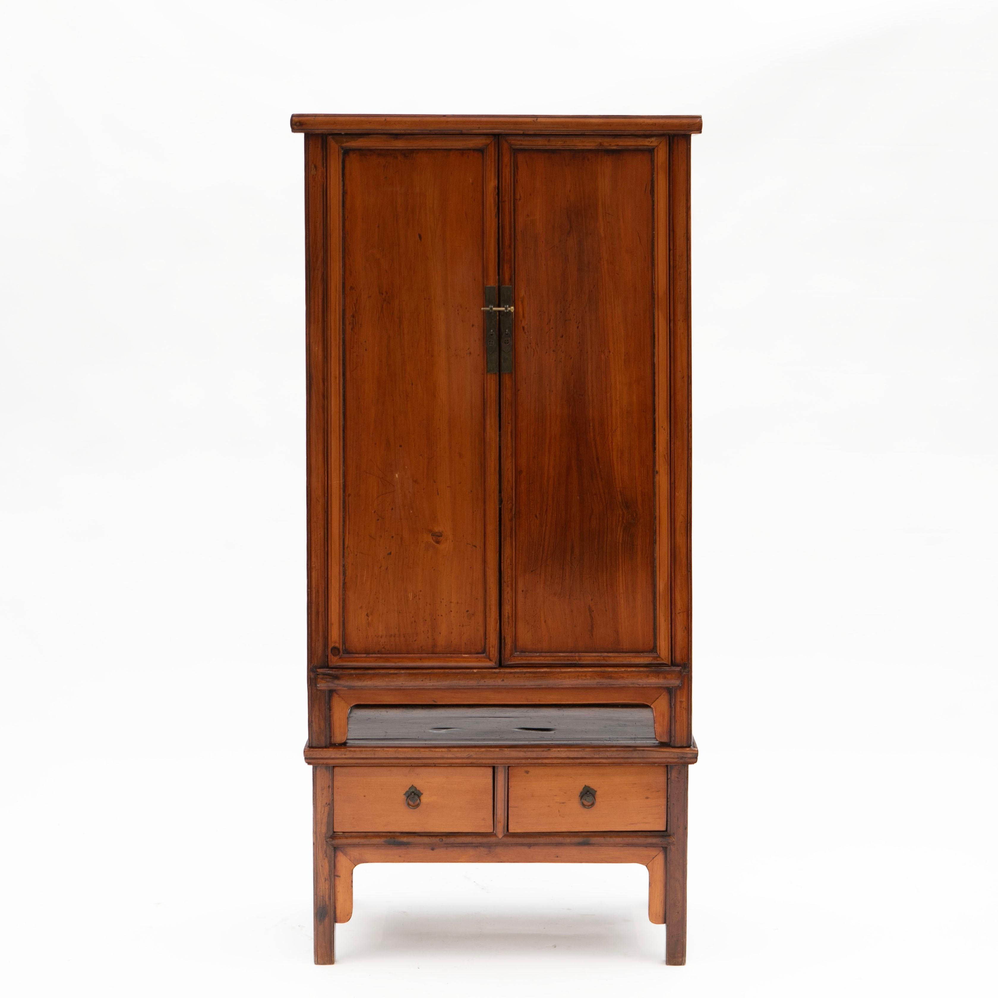 Elegant 19th century Ming style cabinet in crafted in peachwood.

The cabinet is divided into two parts: the upper section, equipped with a pair of doors featuring metal fittings, opens up to an interior of shelves and drawers.
The lower section has
