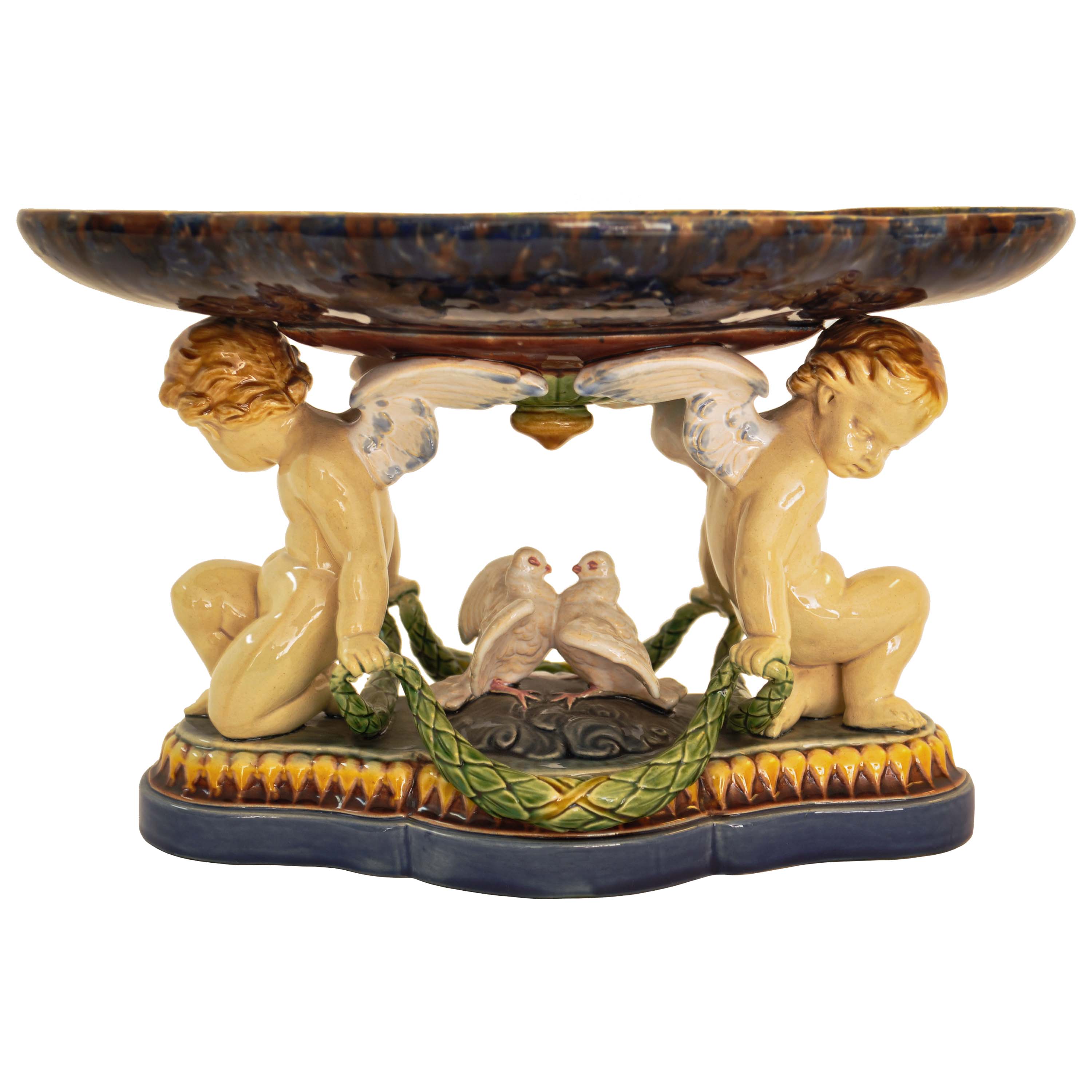 A good antique Minton Majolica centerpiece/tazza, 1861.
The centerpiece with a flanged shaped shallow dish supported with a pair of winged cherubs and a pair of nesting doves and raised on a stepped plinth. The centerpiece having typical Minton