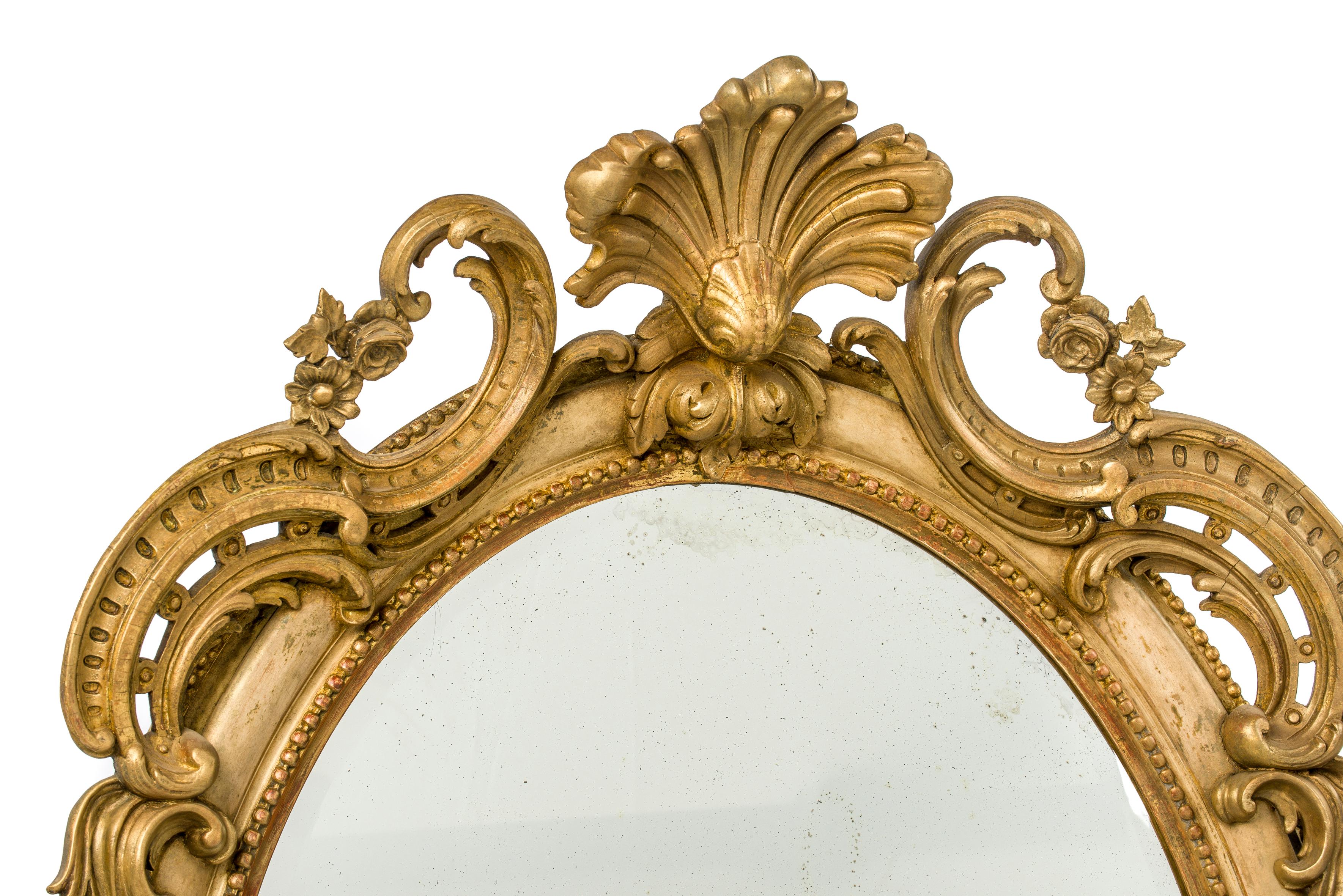 A beautiful large oval mirror with rich ornaments and original facetted mirror plate. 
The mirror has a very warm antique look and feel. The mirror has an ornate top decoration with a central “fleur de lis” with floral elements. At the bottom,
