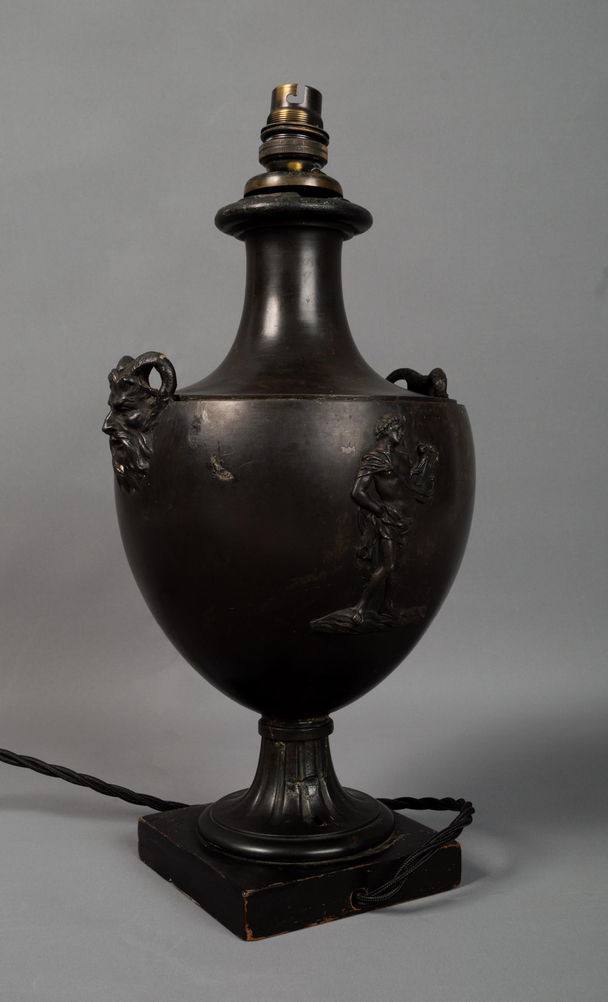 Antique 19th century neoclassical revival vase lamp Germany C.1880.

A Neoclassical style vase converted to a table lamp, black earthenware with faun mask handles, two classical figures in relief to the side, on a circular footed base, mounted on
