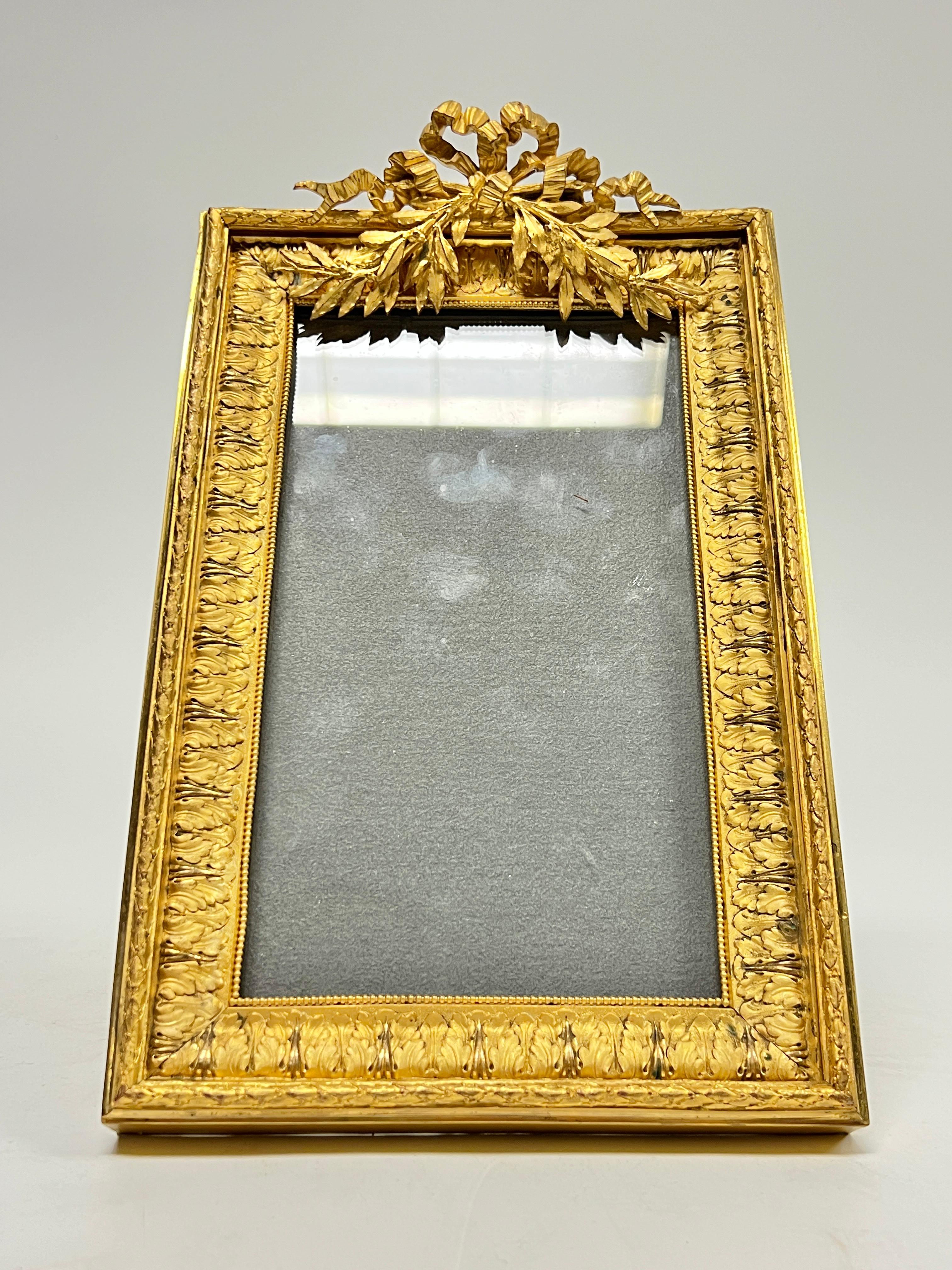 Cadre ancien (19e siècle) de style Louis XVI, exceptionnellement modelé, en bronze doré et moulé, bordé de motifs répétés de feuilles d'acanthe et de baies de vigne, centré d'une couronne et d'un motif de ruban noué en haut.  11 par 6 7/8 par 2 1/4