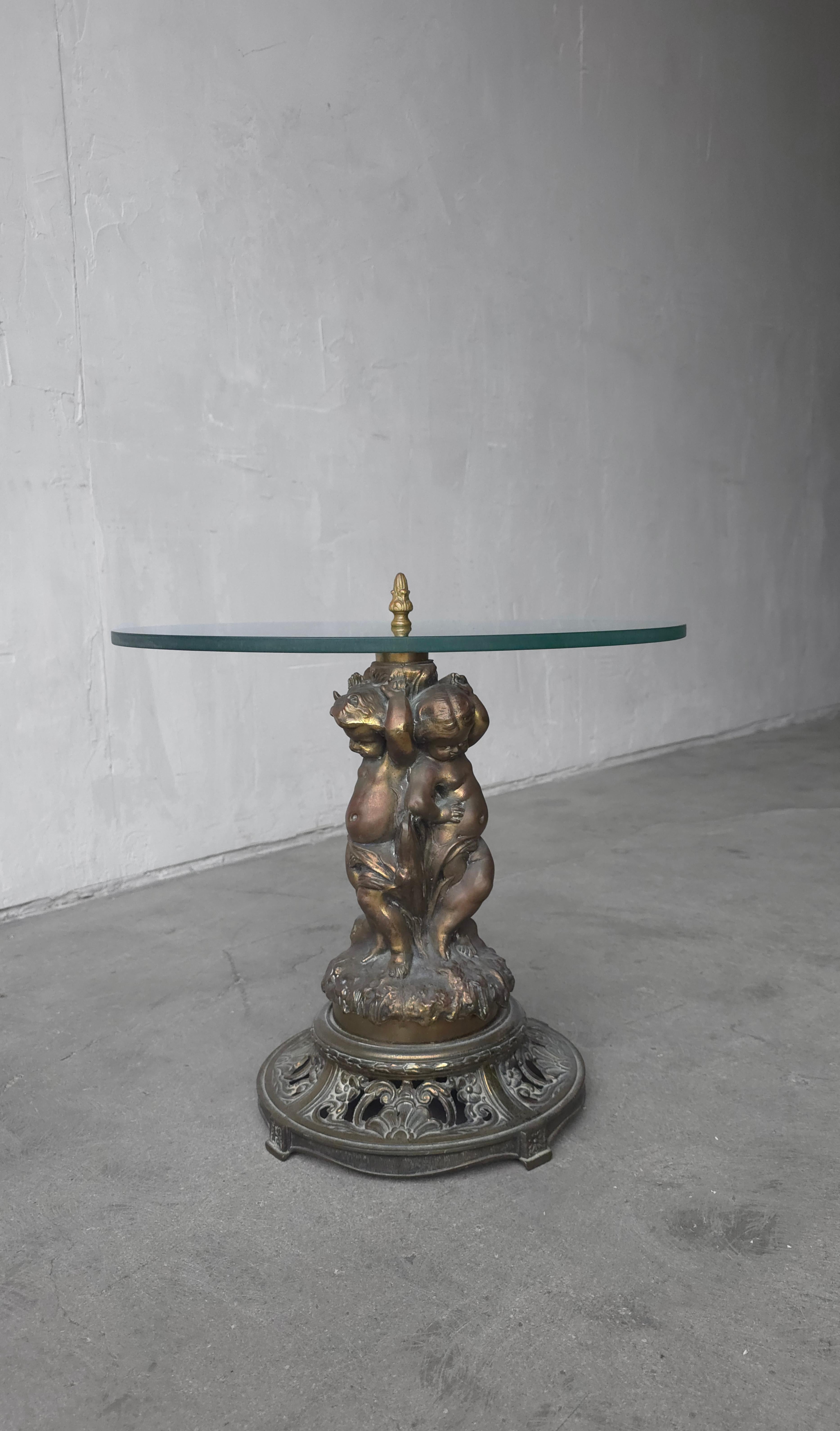 Dieser Tisch ist ein schönes Akzentstück.  Eine Serie von 3 Puttenfiguren, komplett aus massiver, gegossener Bronze, die im Laufe der Jahre perfekt patiniert ist.  Wir lieben es, wie die Glasplatte oben zu schweben scheint, da sie von einem durch