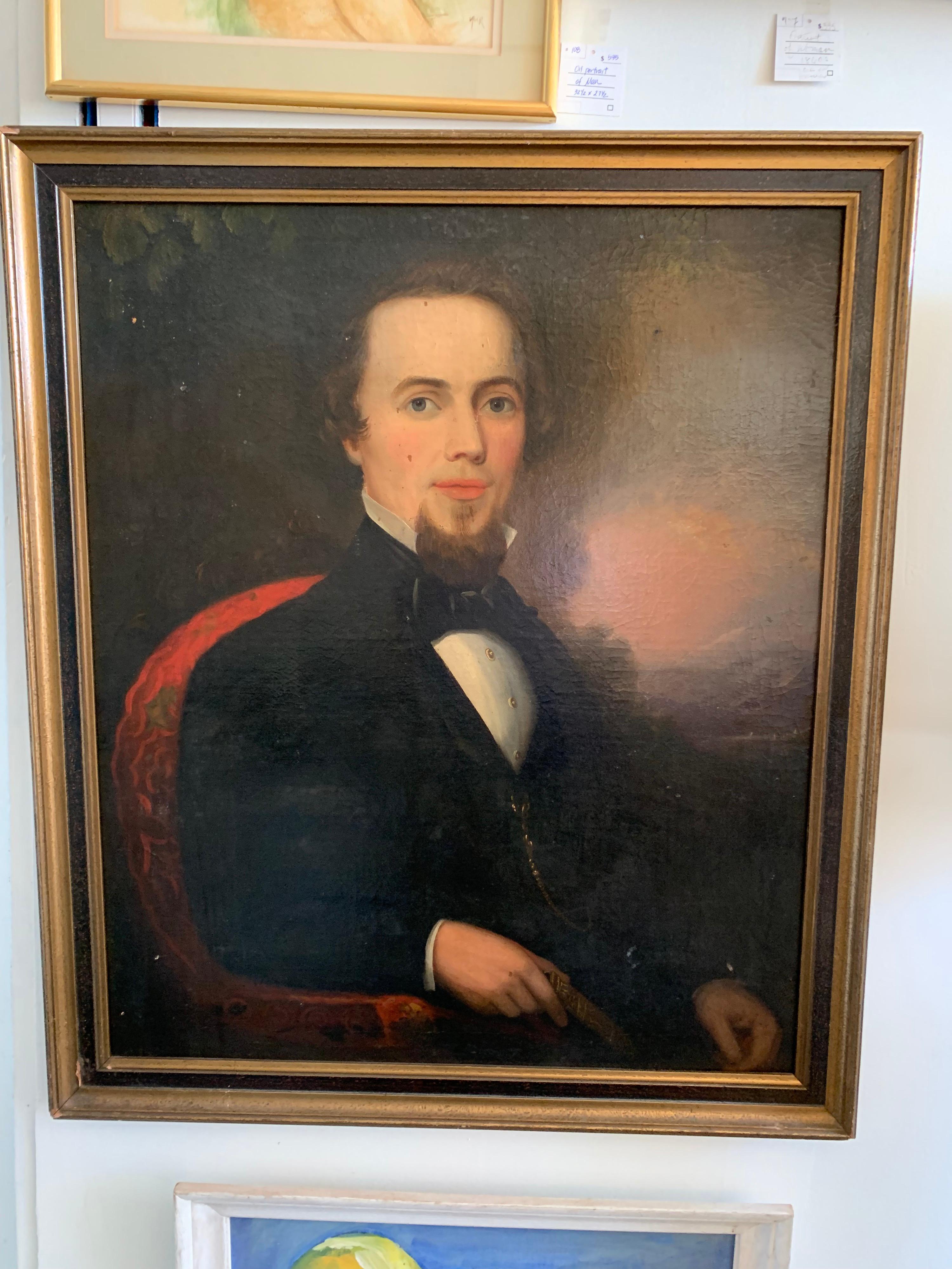 Old original oil painting on board portrait of a man in a black jacket holding a book and seated on a red chair. Unsigned, circa mid-19th century and displayed in a gold gilt frame.