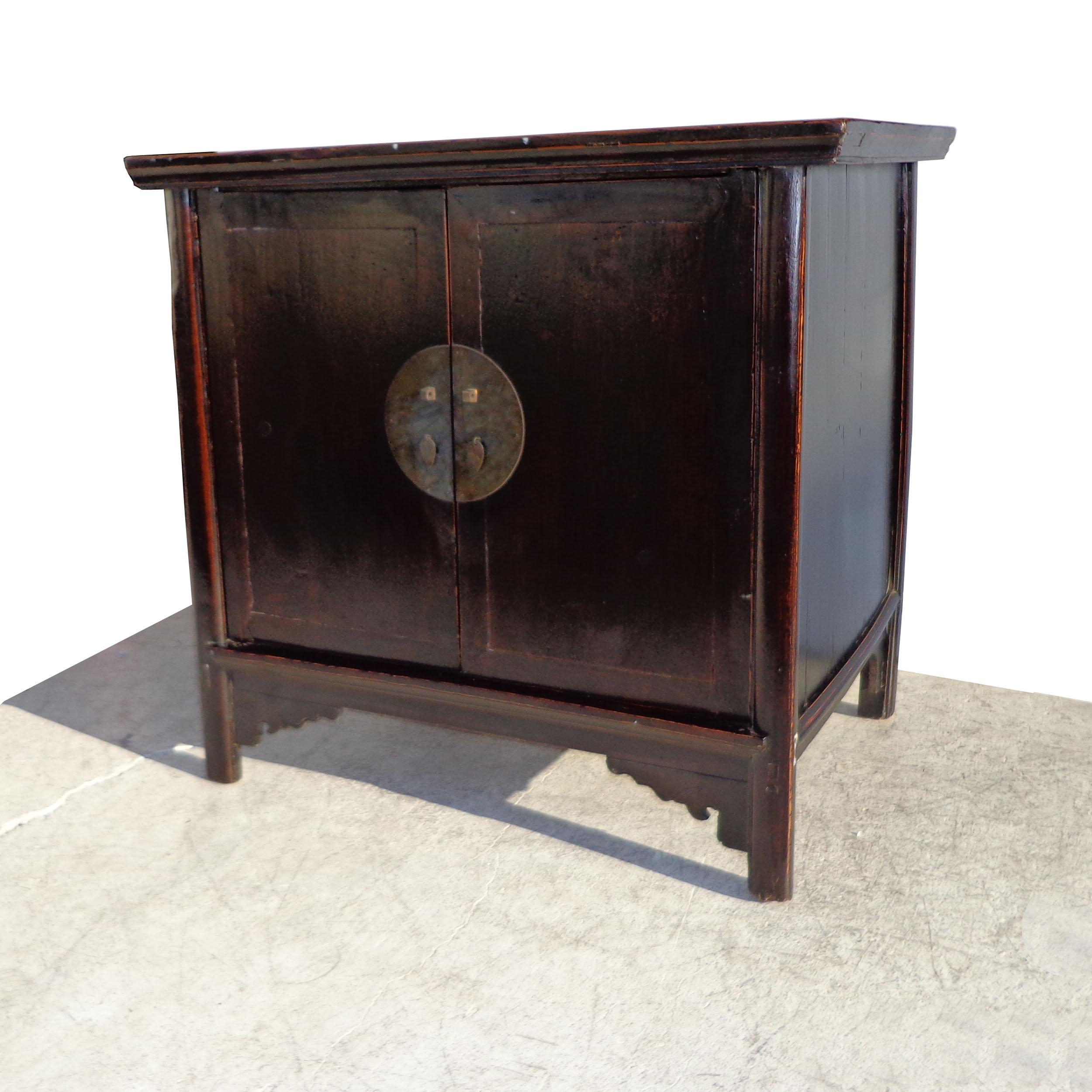 Created in China during the Qing Dynasty, this cabinet features two doors, fitted with a bronze medallion. Four straight legs with carved apron in the front. Beautiful patina in dark elm finish with red undertones.