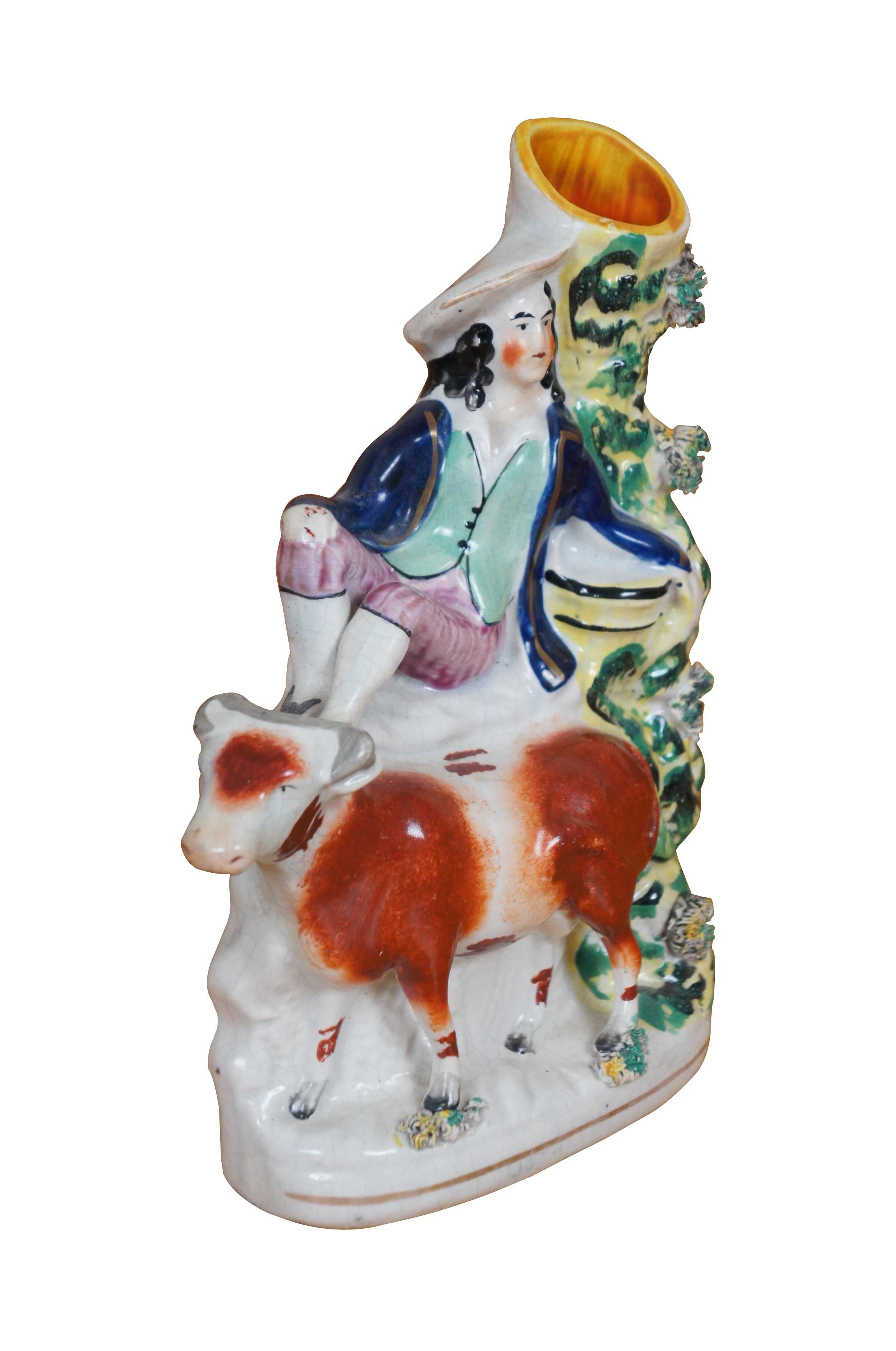 Antique 19th century Staffordshire porcelain flatback figural spill vase depicting a farmhouse scene with male figure recling against a tree with a red and white cow and milk bucket.  This figurine was originally paired with a right facing milk